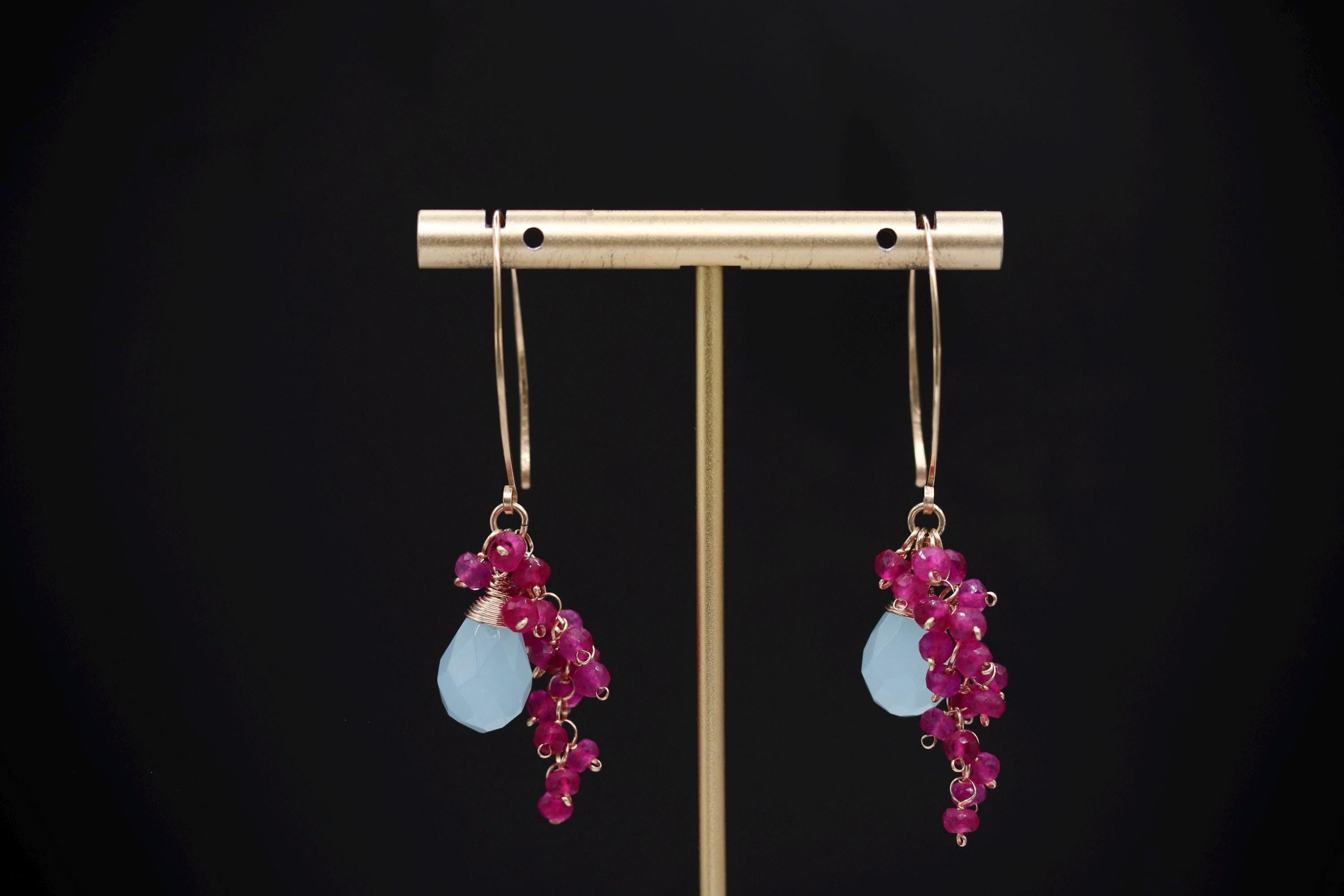 A pair of earrings with blue stones and pink gemstones hanging from the bottom of the earrings.