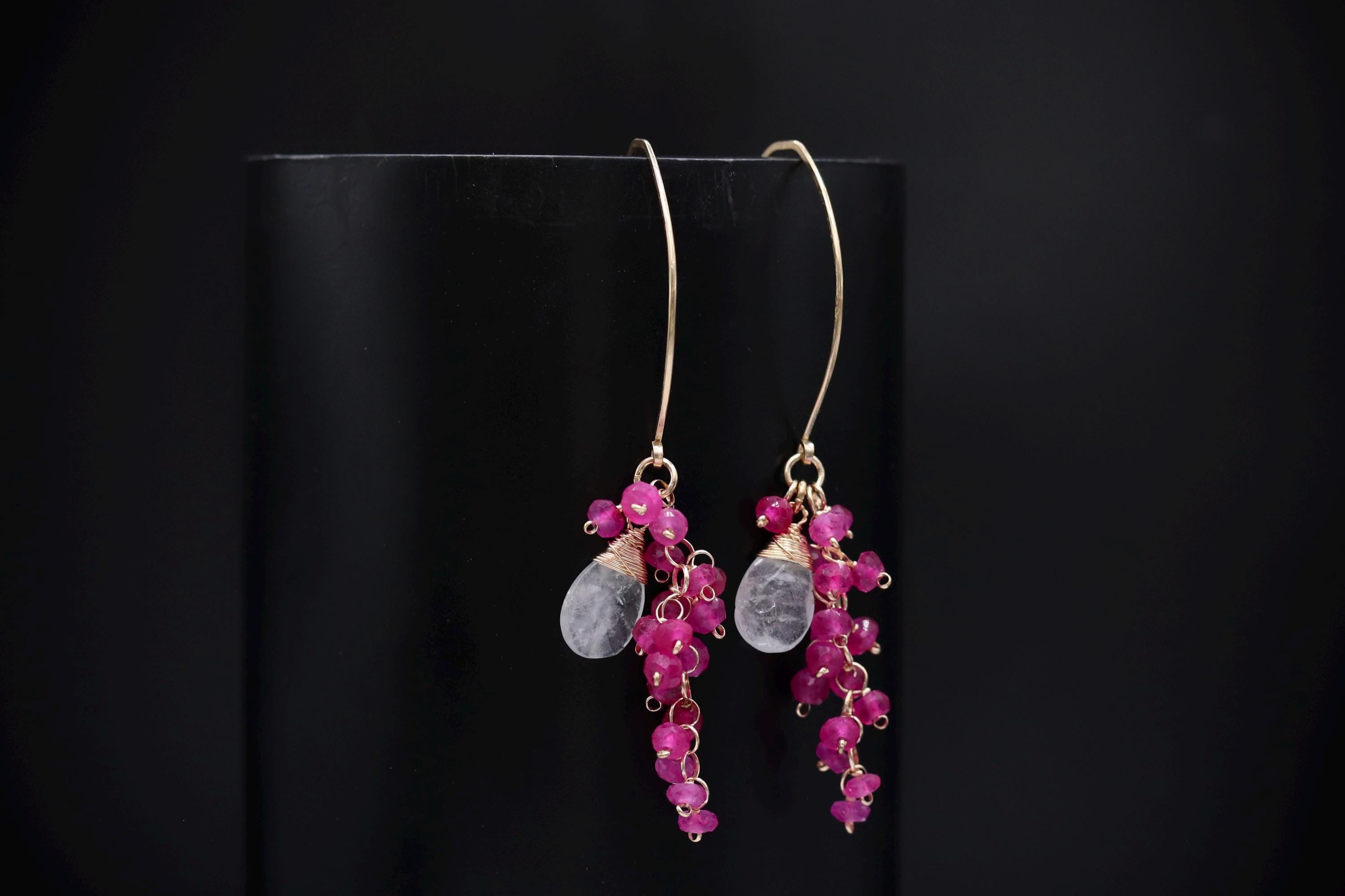 A pair of elegant earrings with a combination of clear gemstones and vibrant pink beads hanging from the ear hooks.