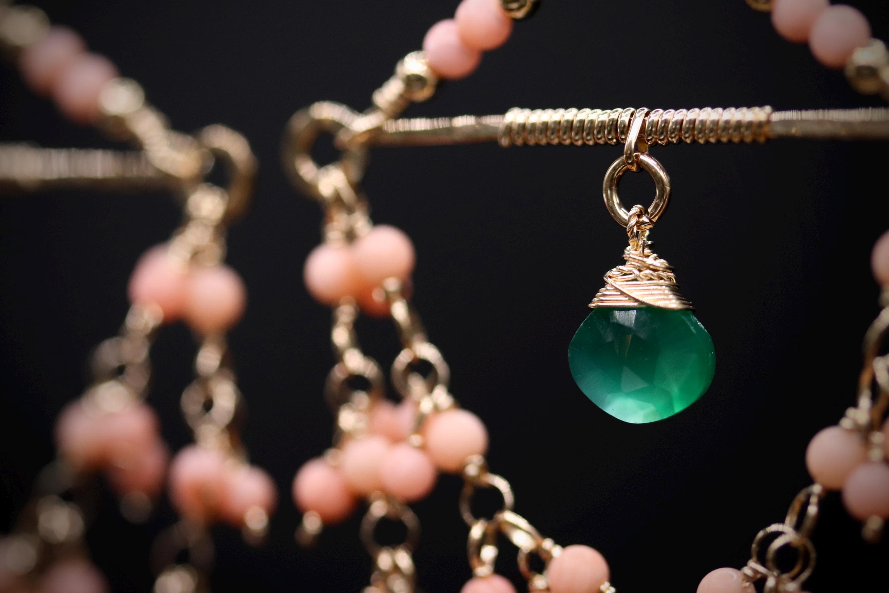 A close-up view of a necklace with a green gemstone pendant, surrounded by a chain of pink beads.
