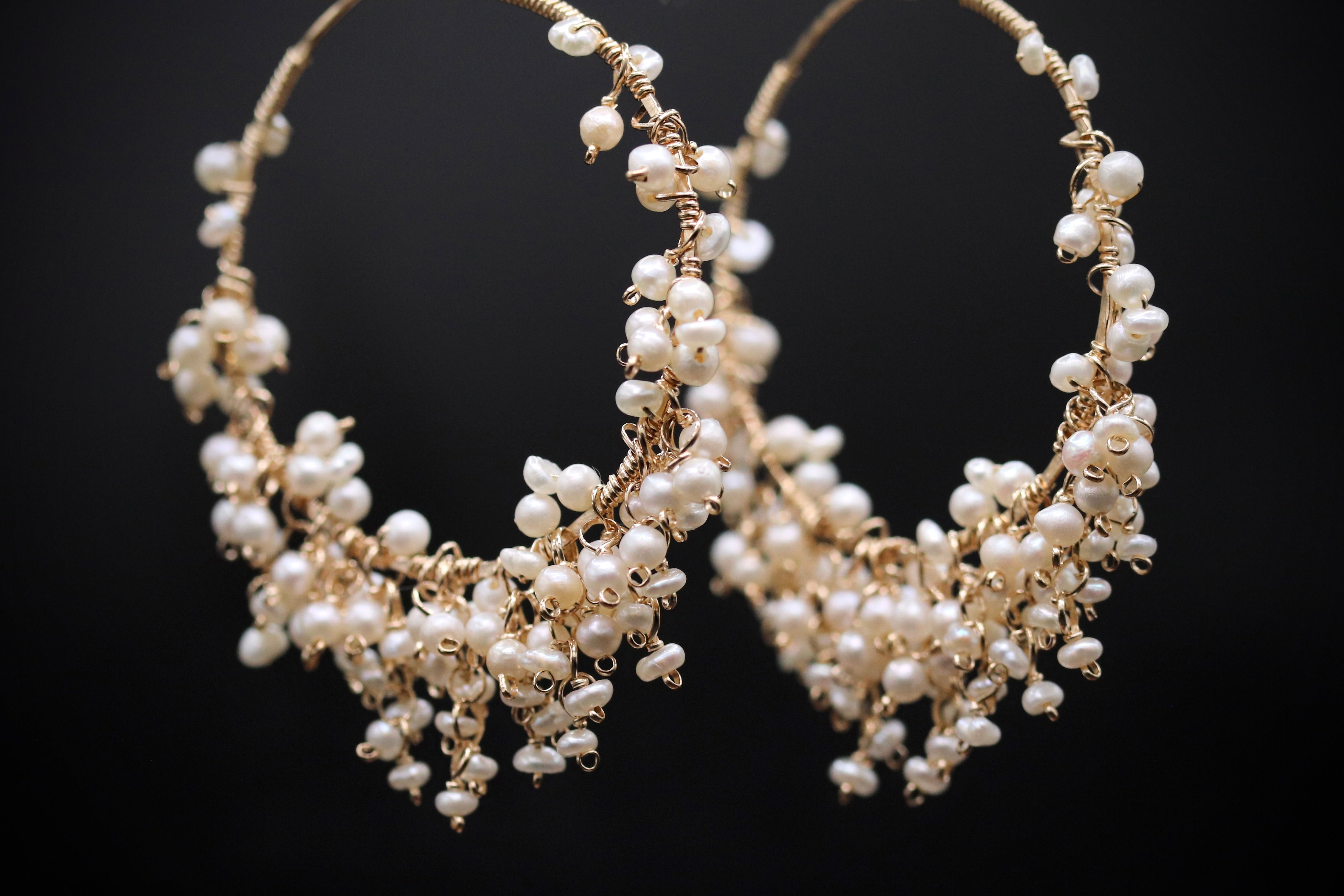 A pair of elegant gold hoop earrings adorned with numerous small white pearls, creating a delicate and sophisticated design.