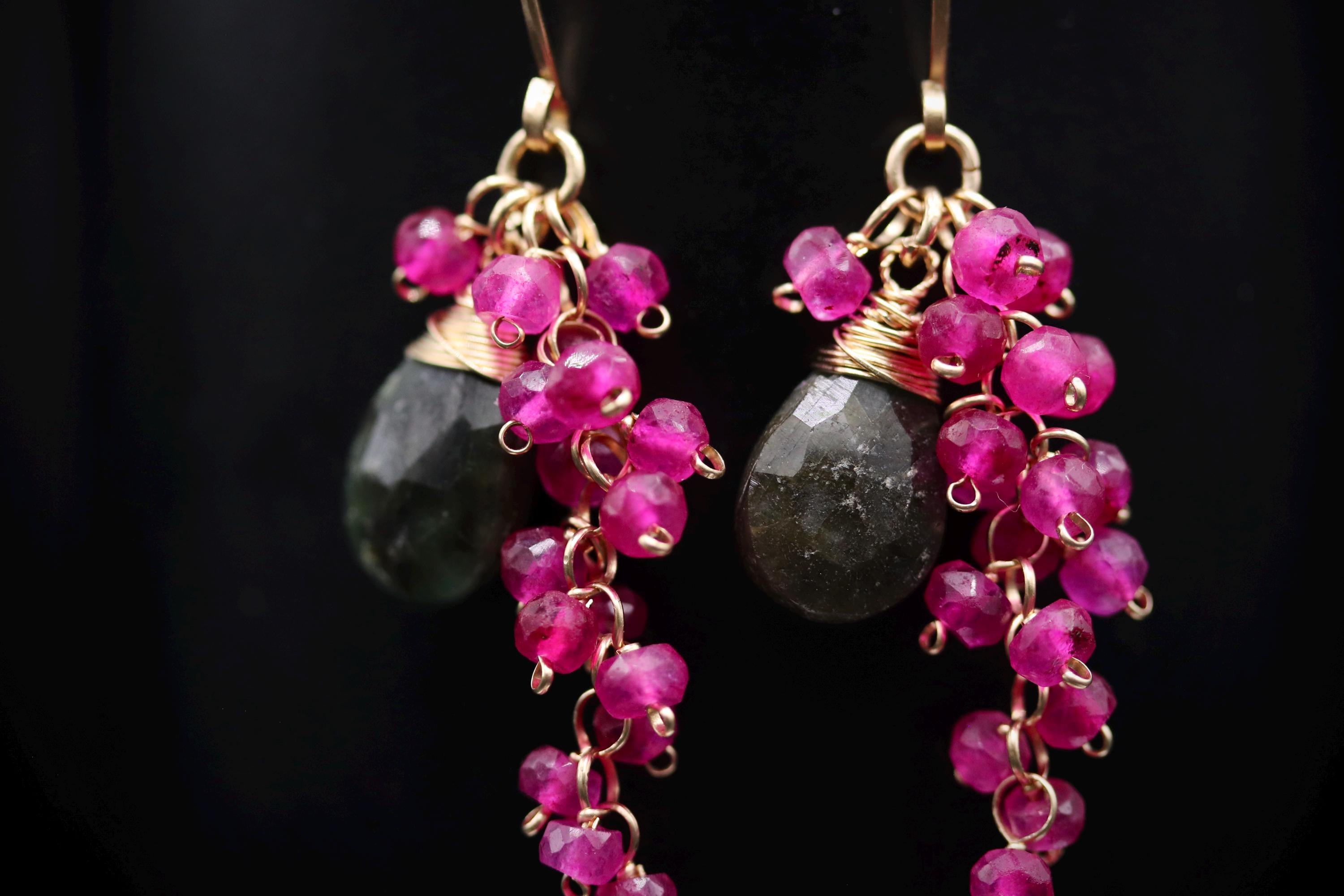 A pair of earrings with dark green stones and pink beads hanging from the ear hooks.