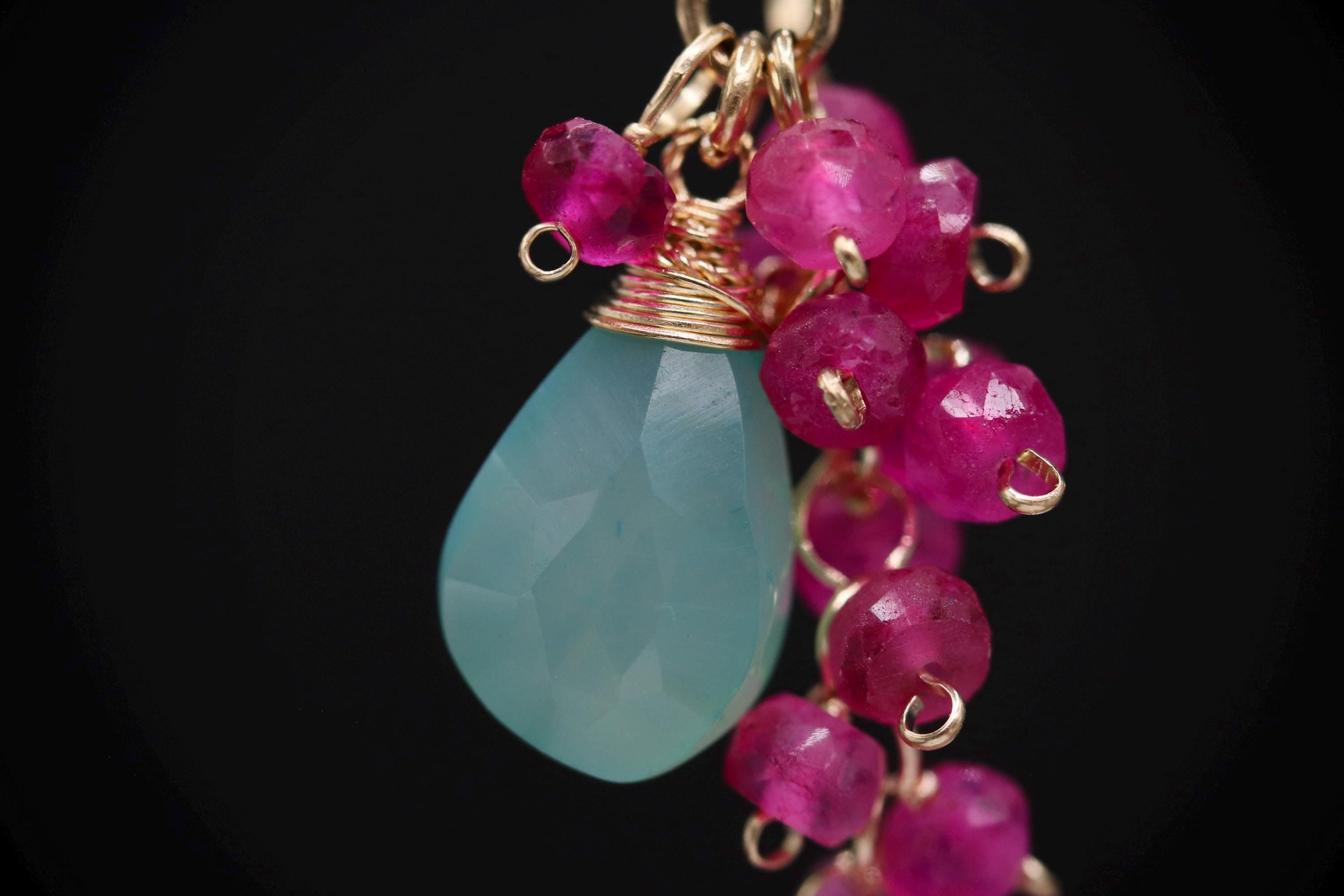 A close-up image of a light blue stone pendant with a chain of small, round, pink gemstones.