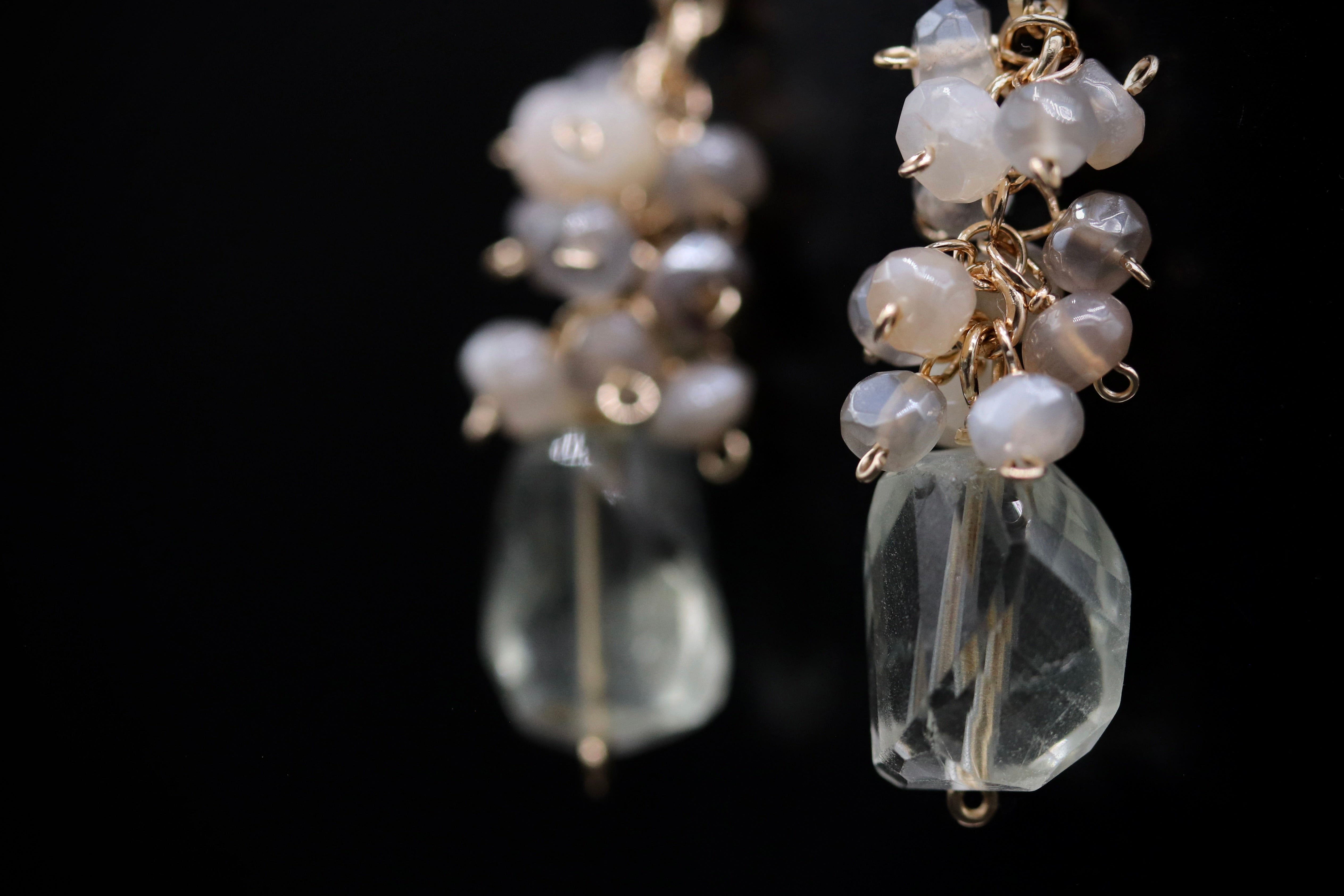 A close-up view of a pair of delicate earrings with clear gemstone accents and metal chains.