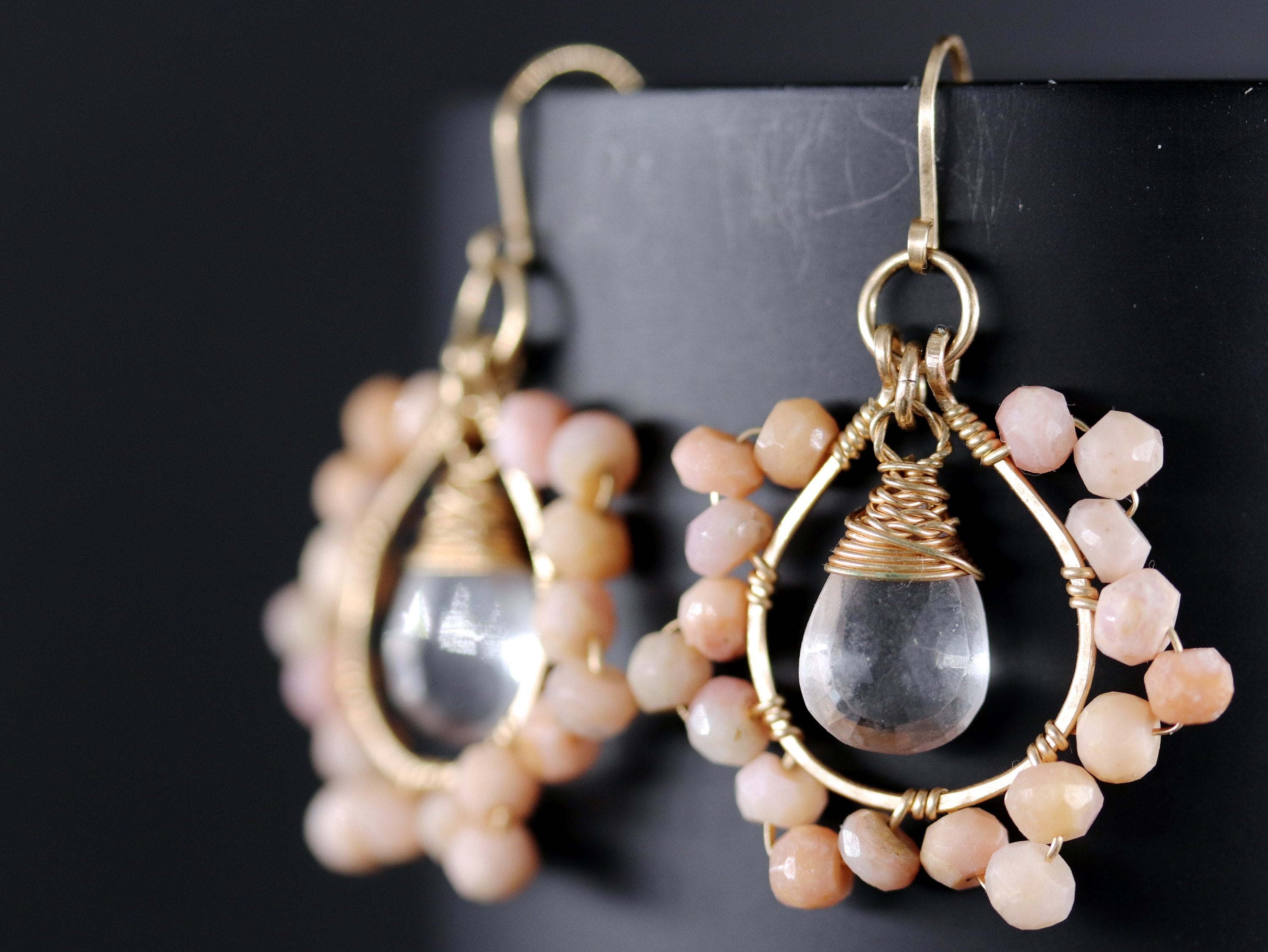 May include: Gold earrings with a clear teardrop-shaped crystal and a circle of pink opal stones.
