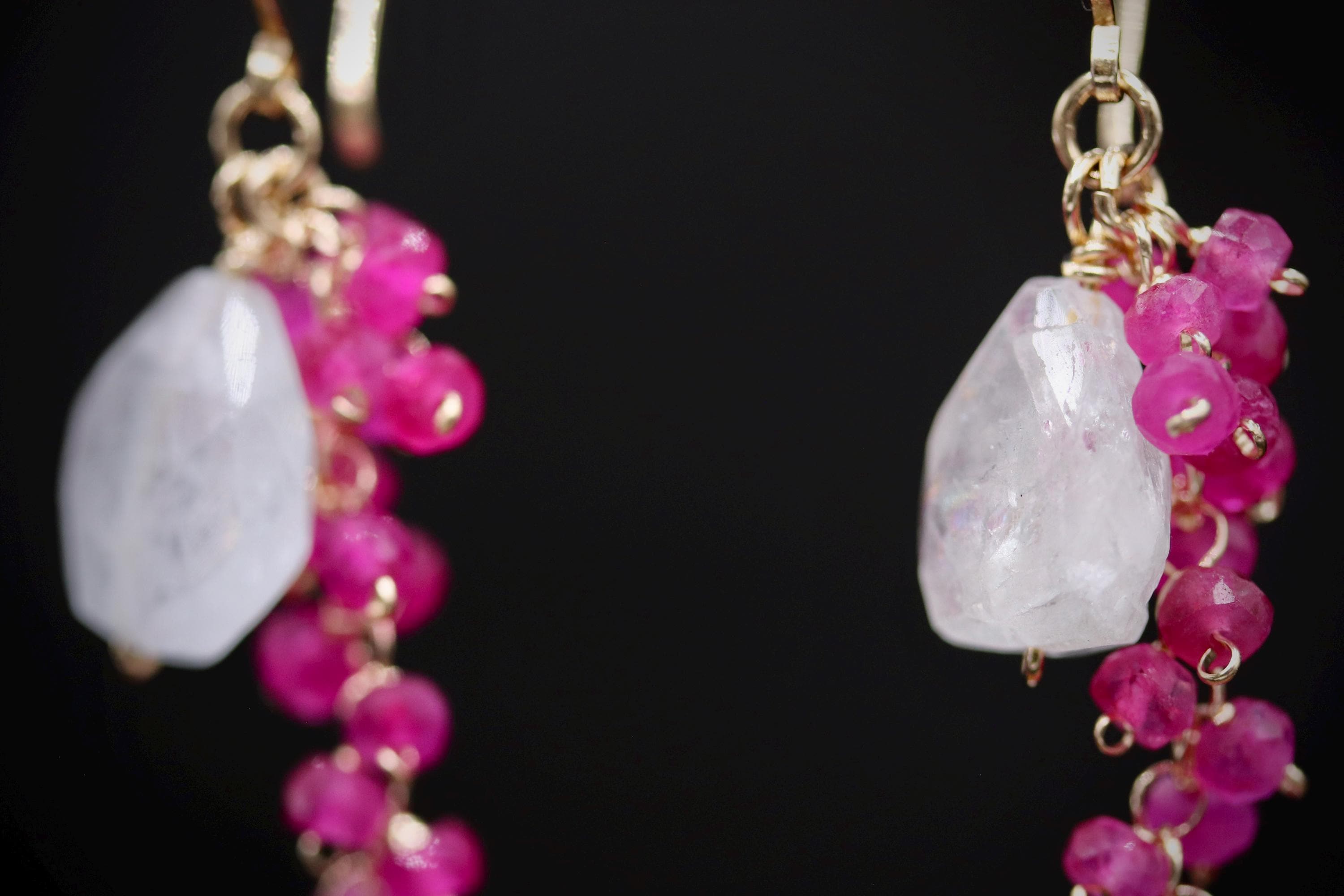A pair of earrings with a combination of white and pink gemstones, as well as small, dangling beads in a metallic color.