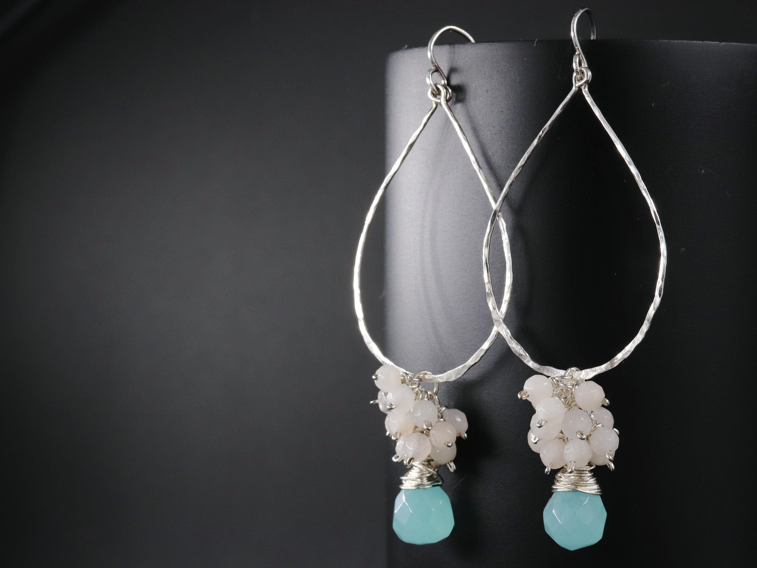 May include: Silver teardrop earrings with a cluster of light pink and white stones and a single light blue stone at the bottom.