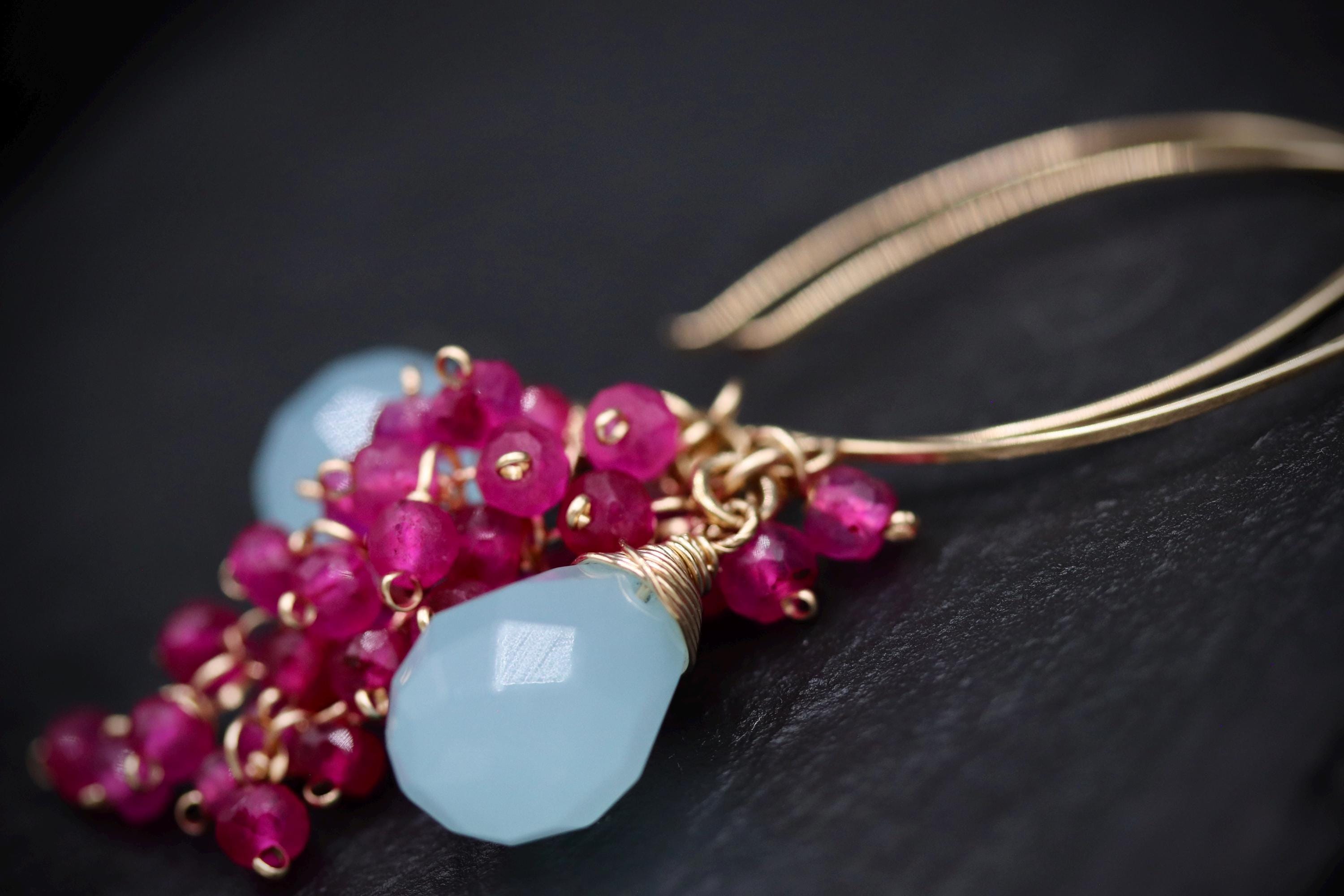 A close-up image of a piece of jewelry, featuring a combination of blue and pink gemstones, as well as a gold chain or cord.