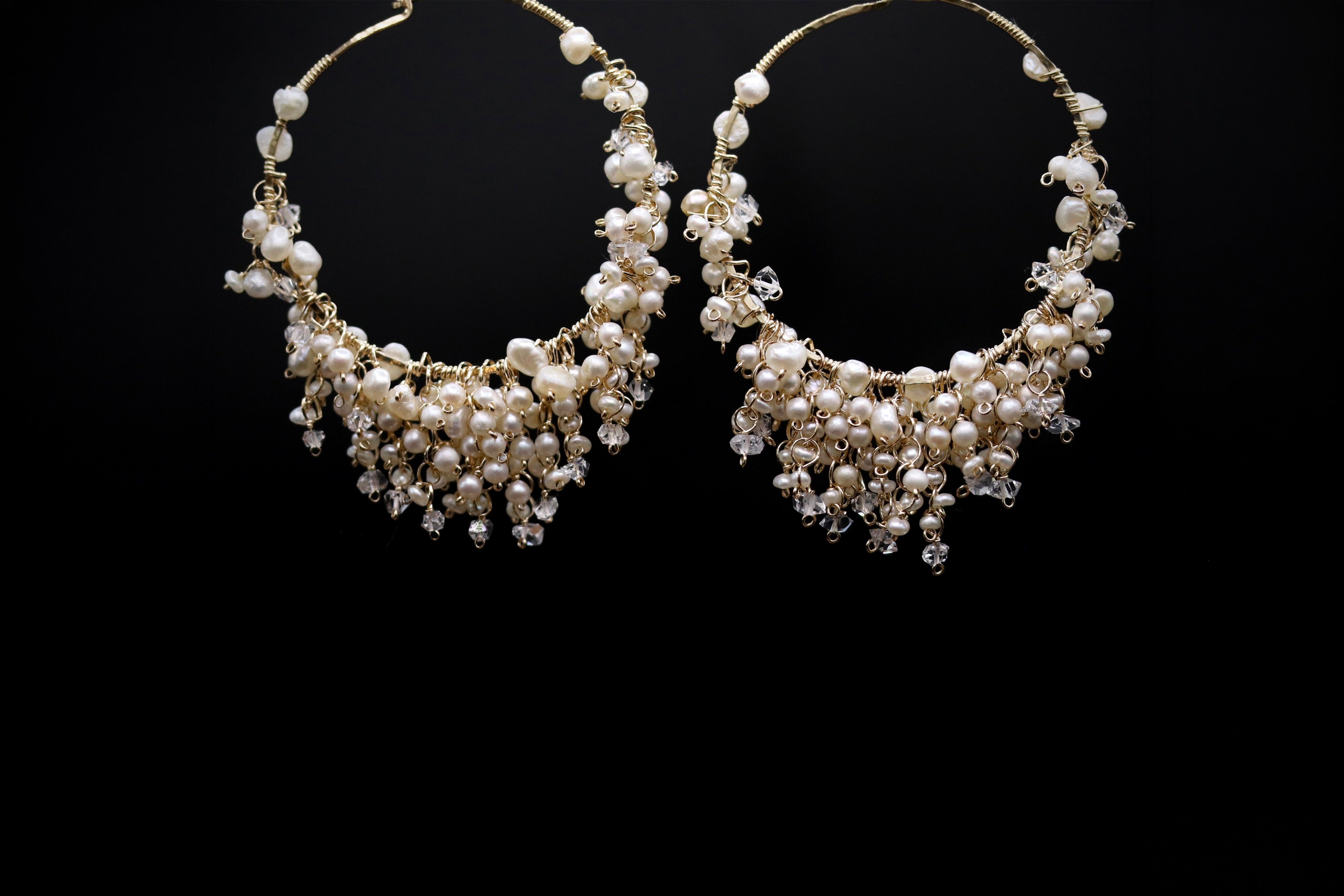 A pair of elegant earrings with a delicate, dangling design made of small white pearls and crystal accents against a black background.