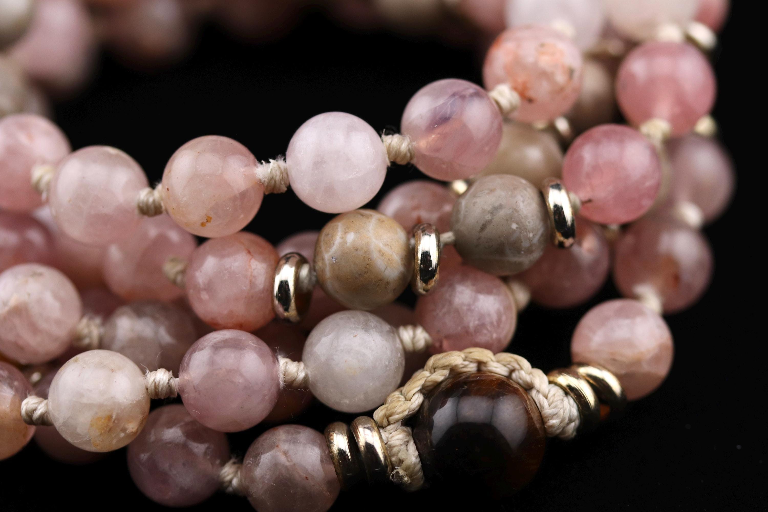 A close-up image of a beaded necklace with various colored stones, including pink, gray, and black stones, and metal clasp.