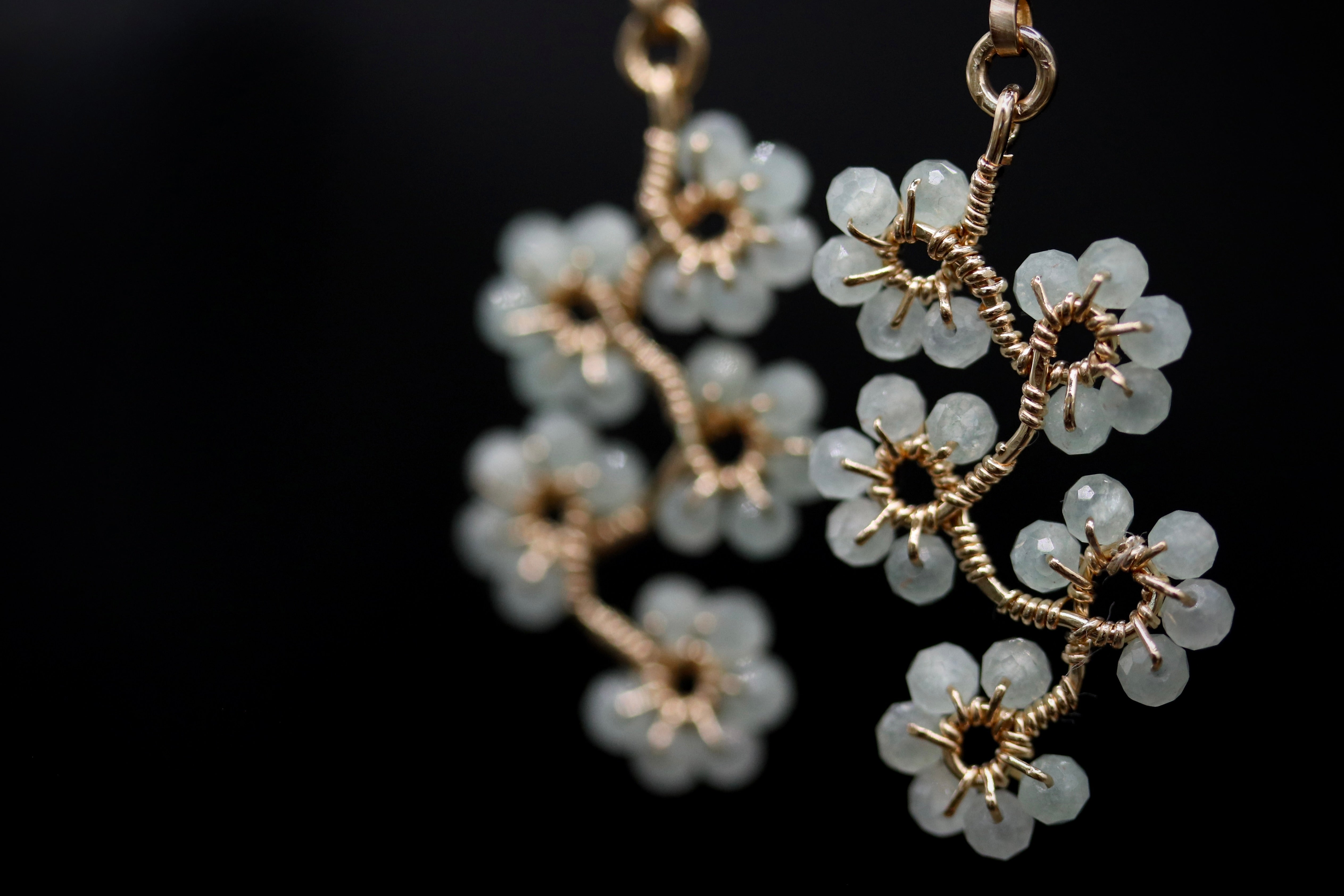 A close-up view of delicate earrings with white, crystal-like stones arranged in a floral pattern against a dark background.