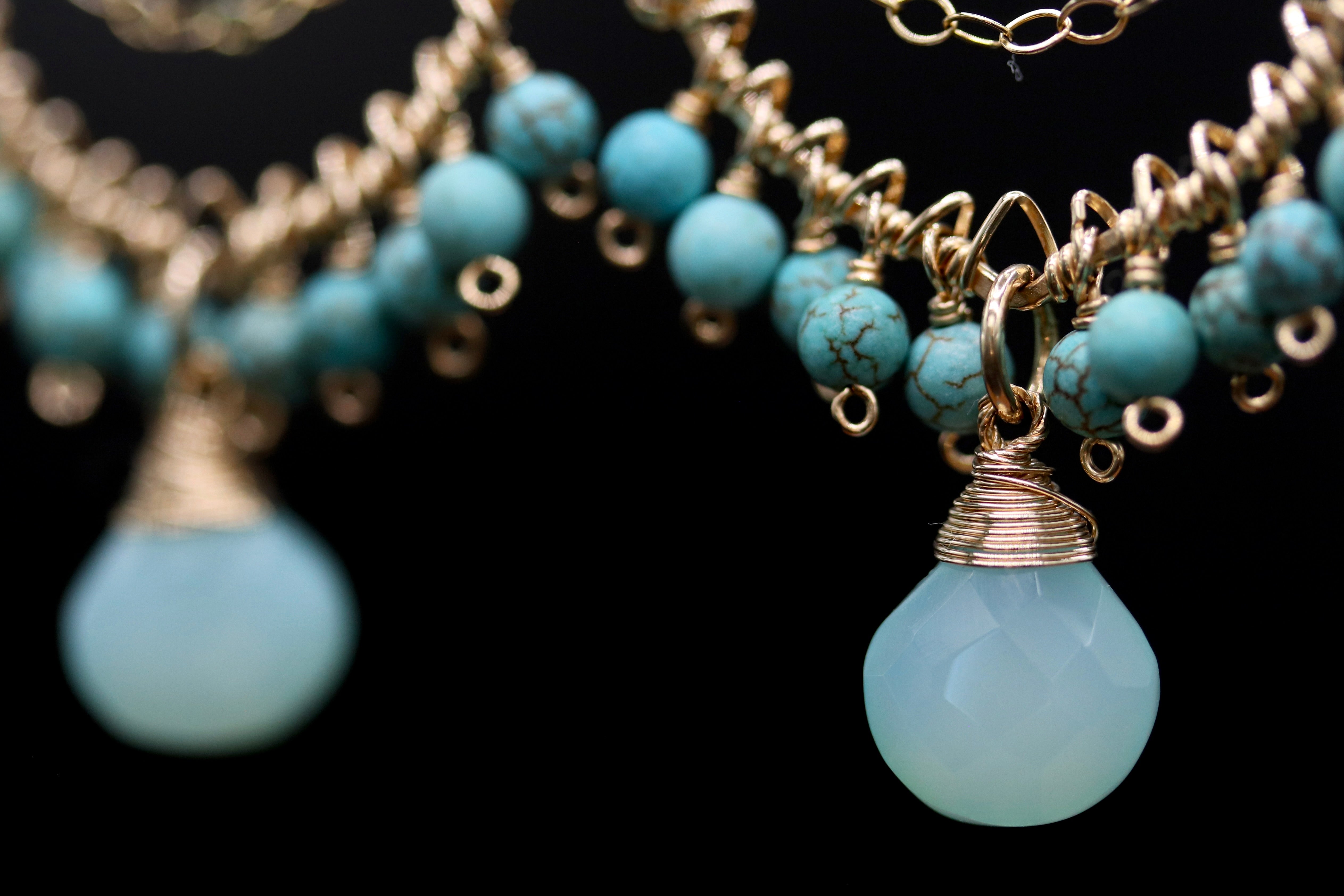 A close-up view of a necklace with turquoise beads and gold-colored metal pendants.