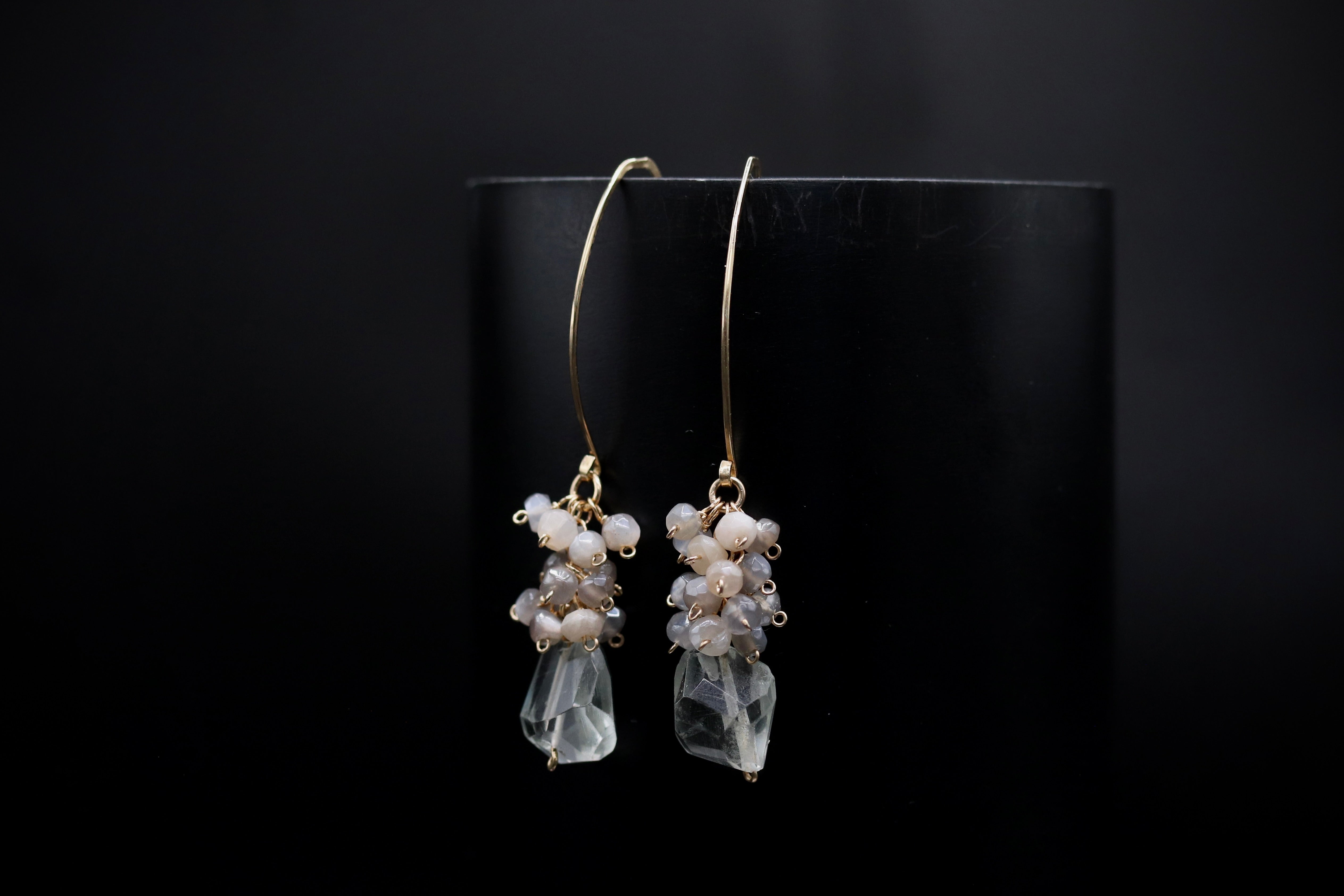 A pair of elegant earrings with clear gemstone accents and dangling gold hooks, displayed against a dark background.