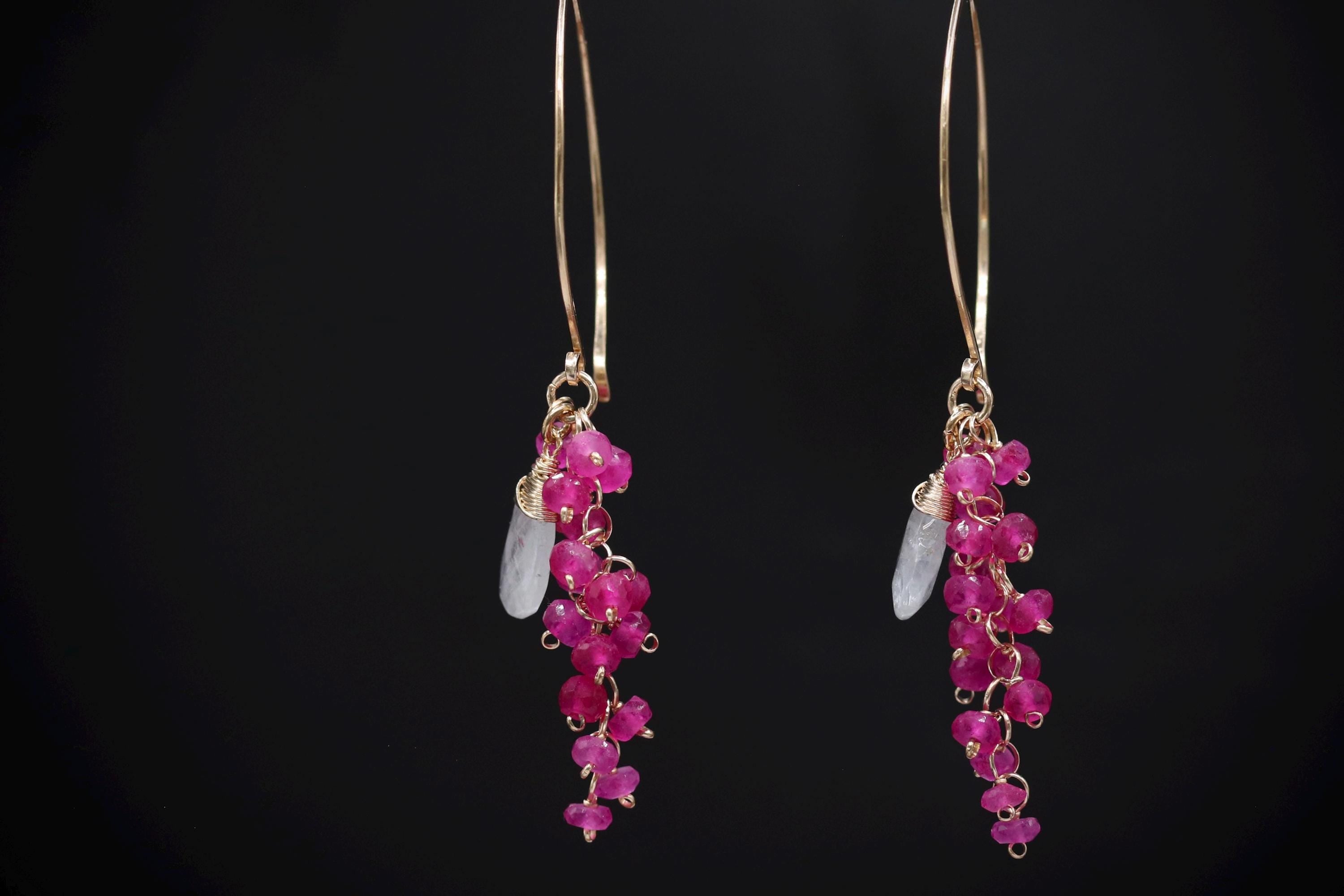 A pair of earrings with a combination of pink gemstones and white stones, hanging against a black background.