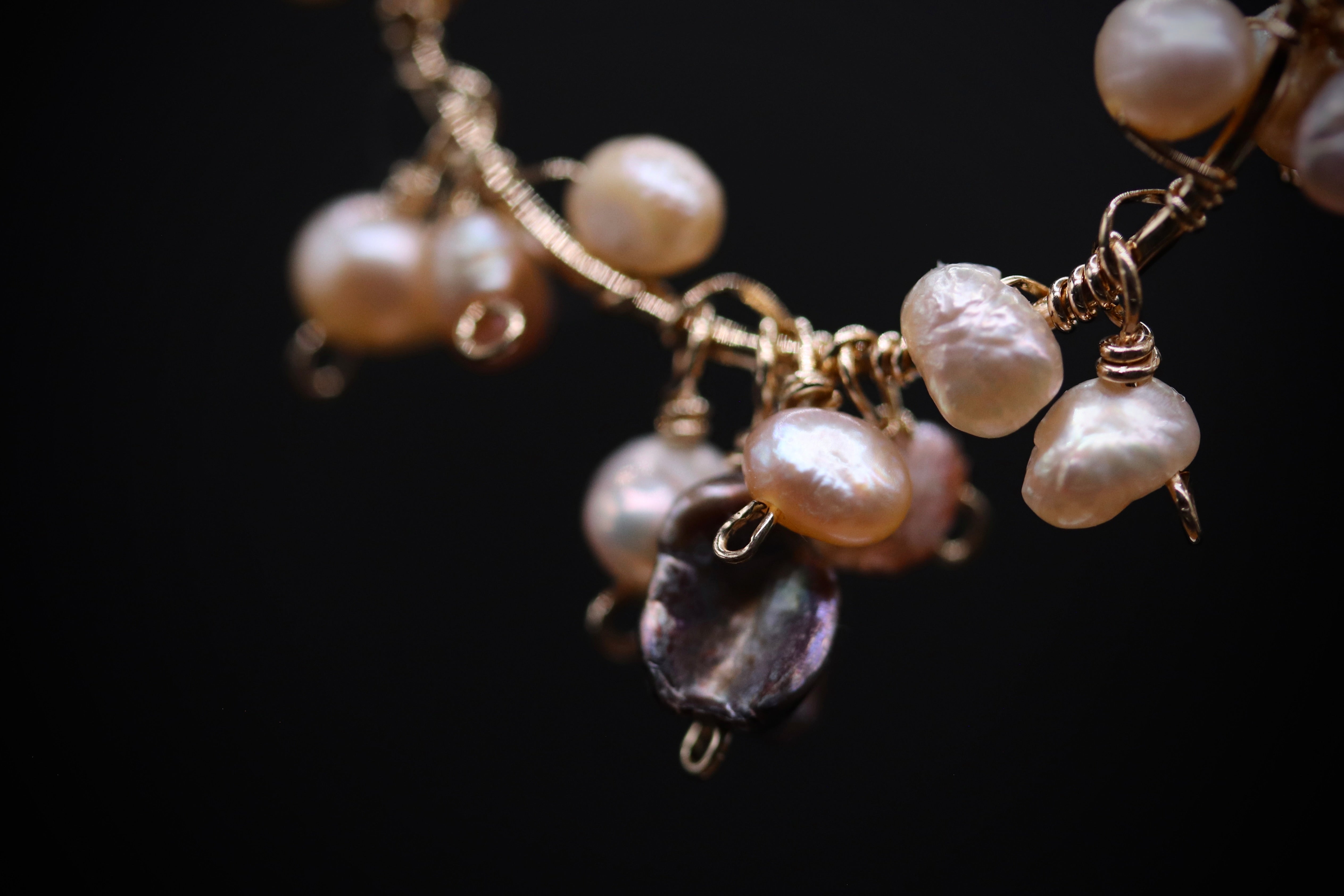 A close-up view of a delicate necklace with a combination of white and purple pearls, as well as some small, round beads, against a dark background.