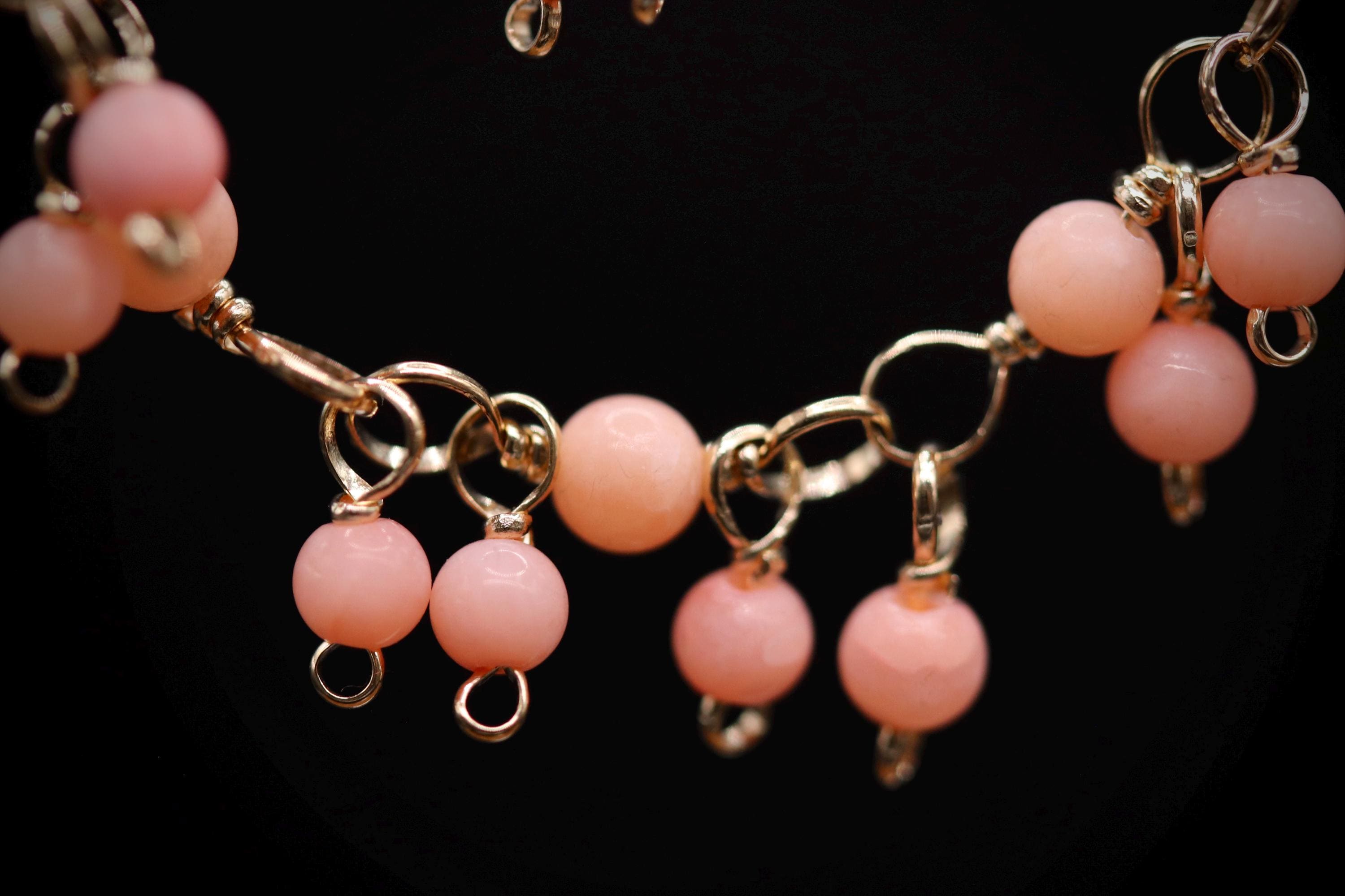 A close-up view of a necklace with a chain of small, round beads in a soft pink color, and dangling earrings with similar beads.