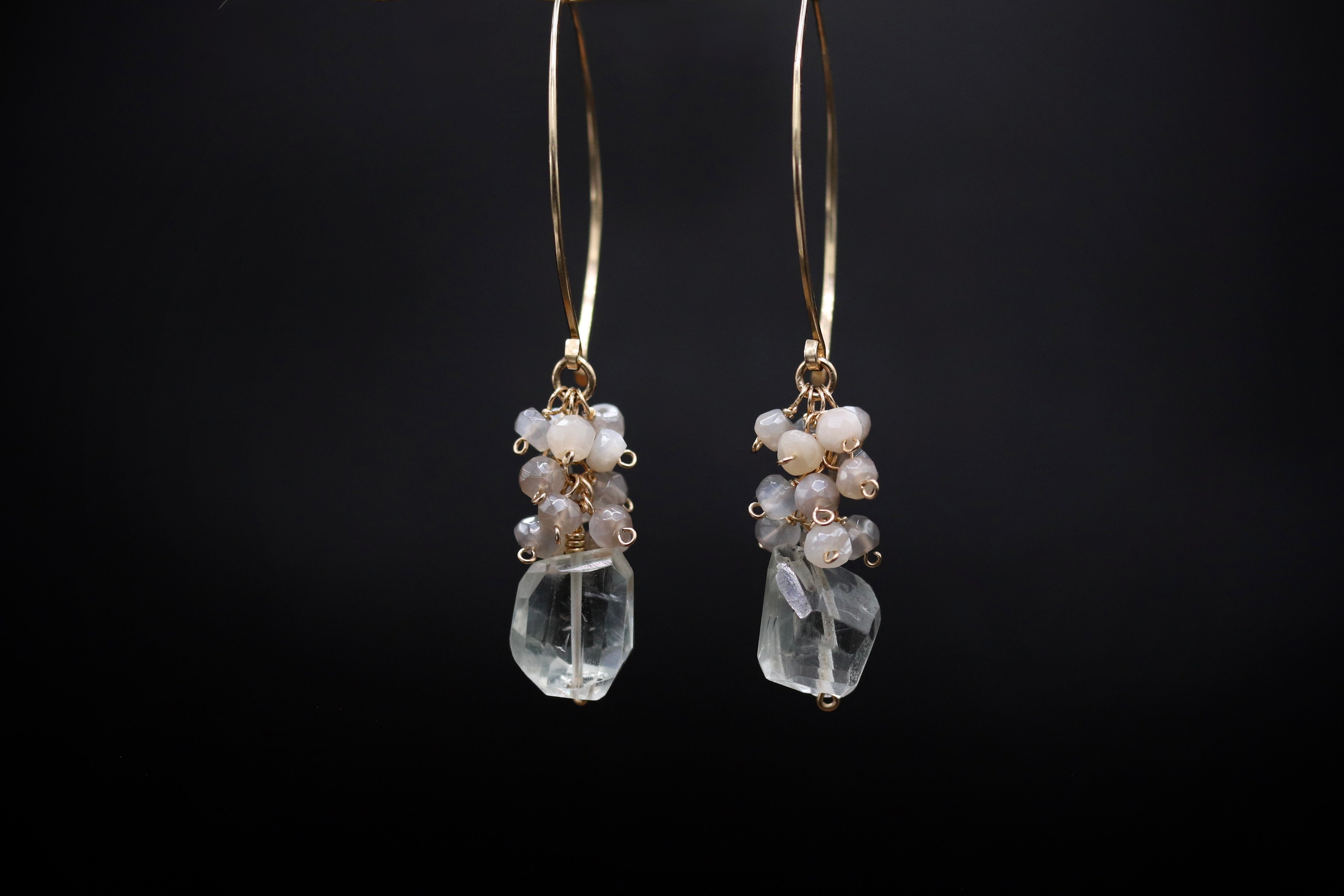A pair of elegant earrings with clear gemstone accents and metal hooks, displayed against a dark background.