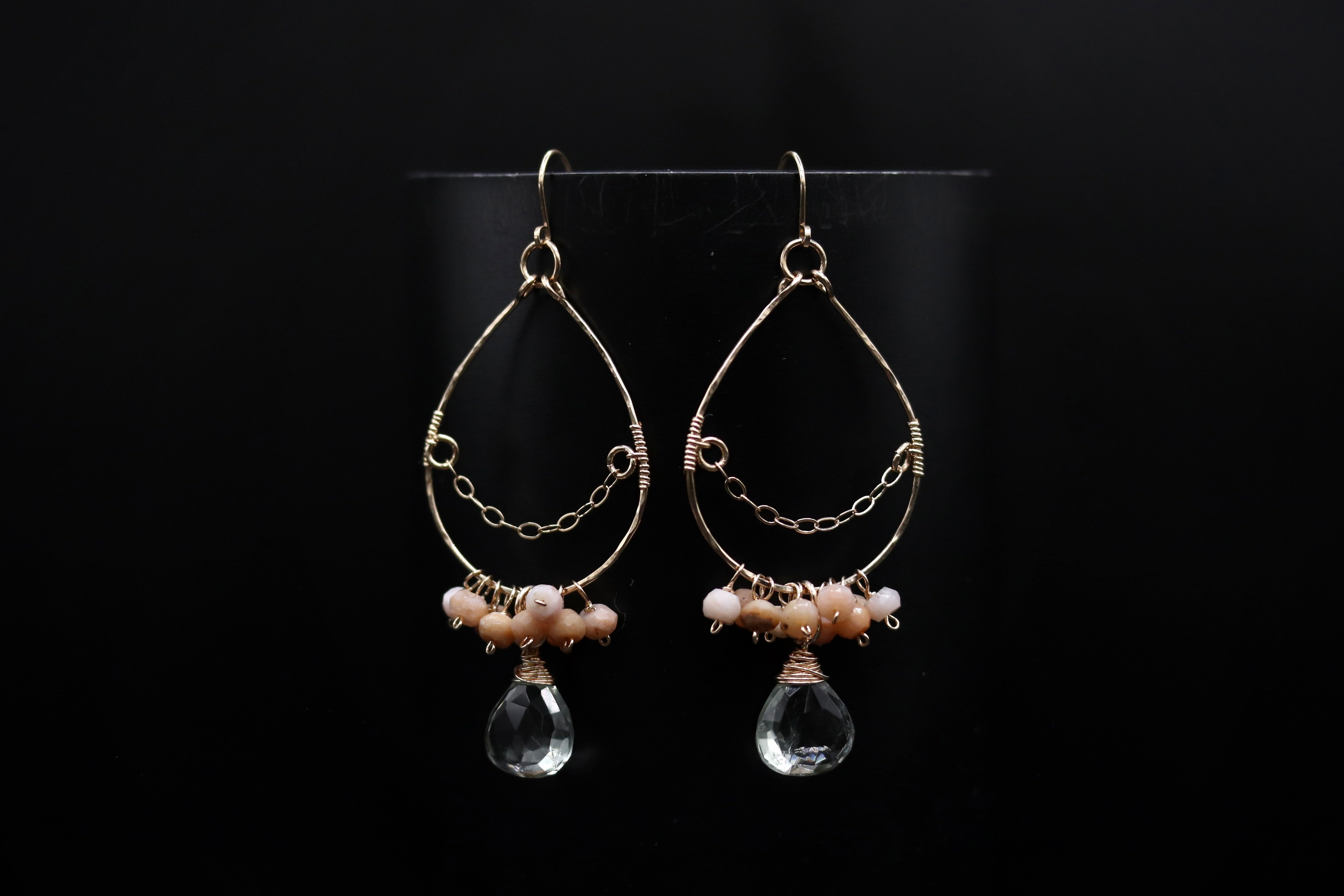 A pair of elegant earrings with a clear crystal pendant and beaded accents, displayed against a black background.