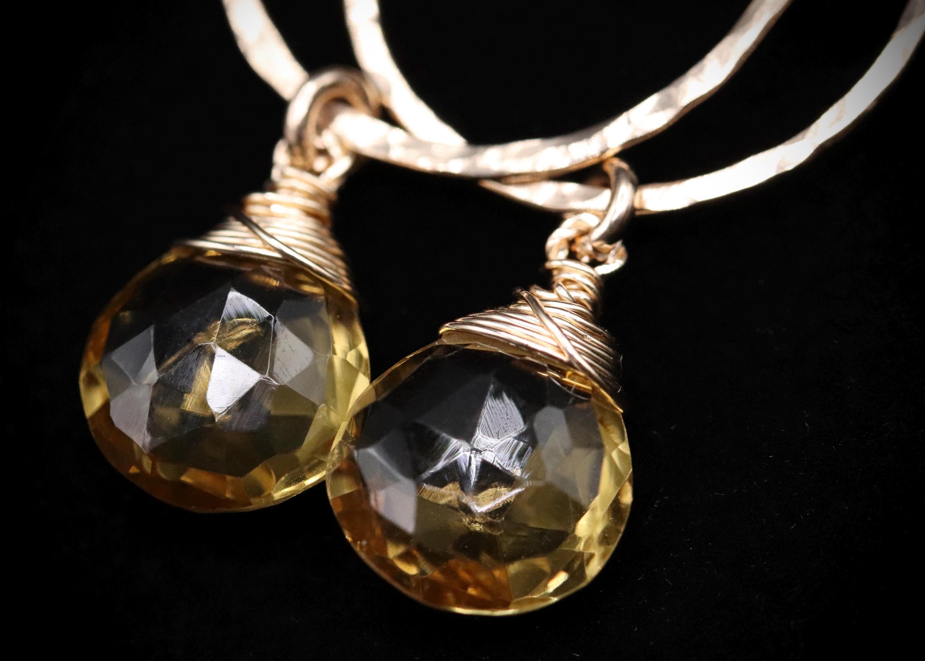 A pair of elegant gold-colored earrings with clear gemstone-like stones, set in a twisted metal frame, against a dark background.