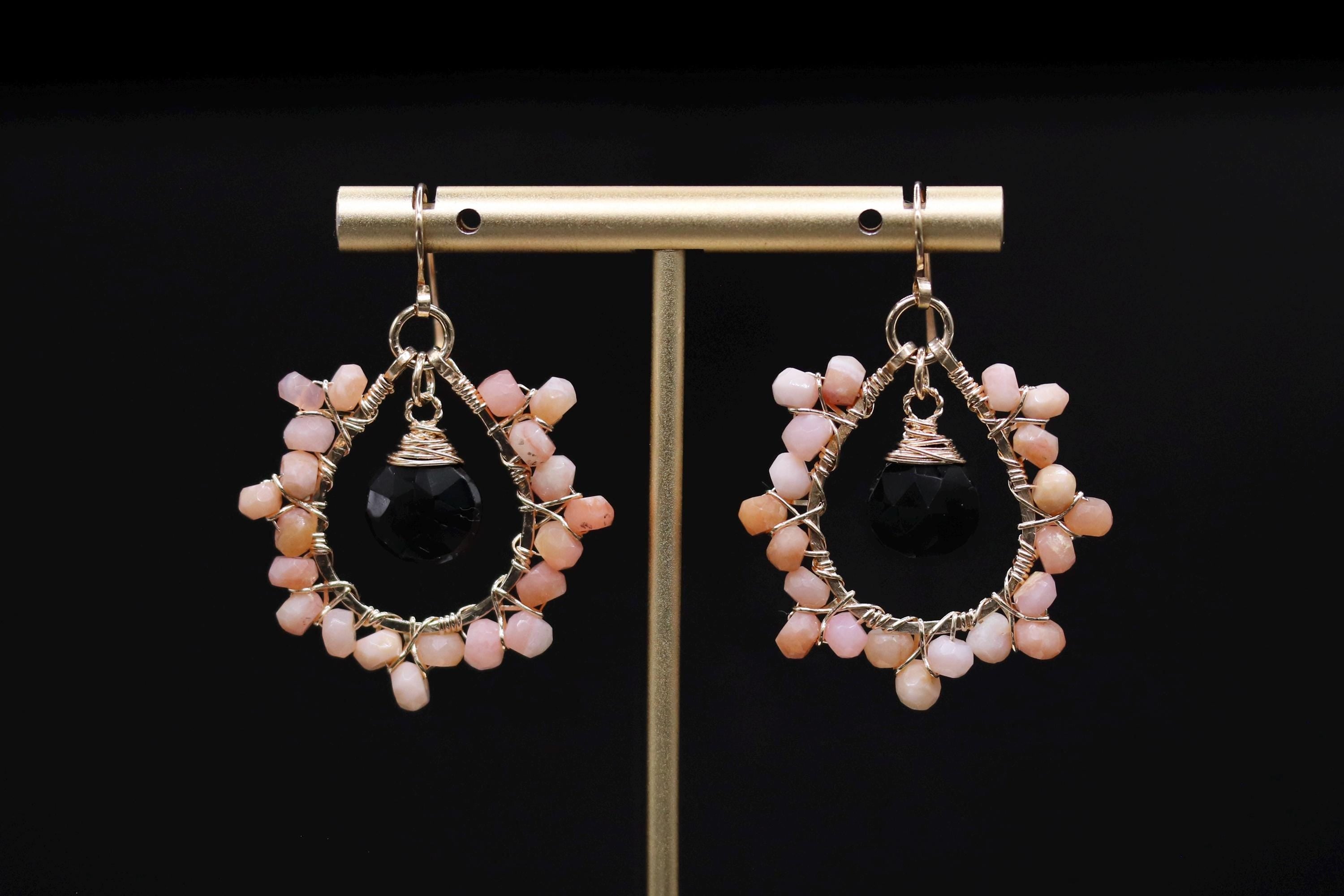 A pair of earrings with black and pink beads, hanging from a gold stand.