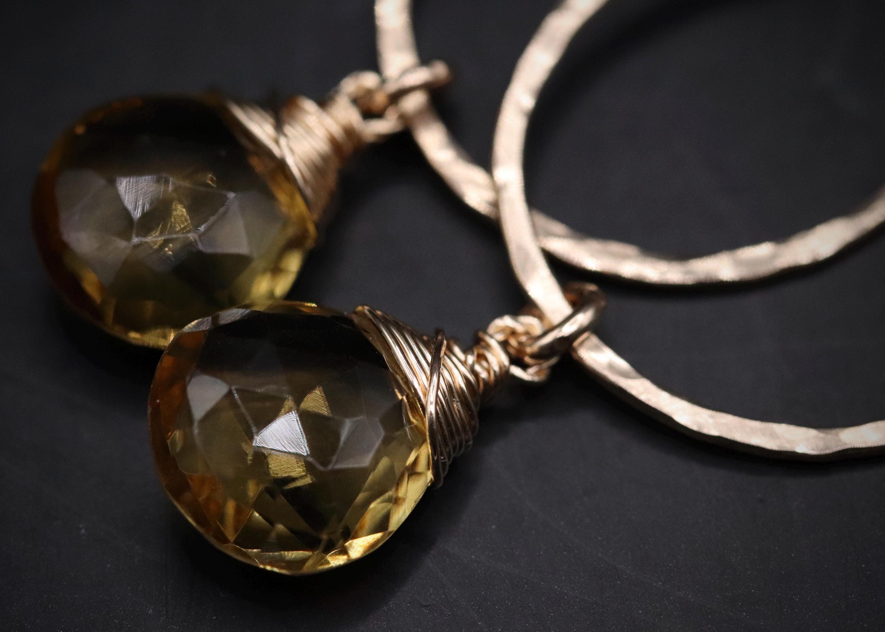 A pair of gold-colored earrings with large, clear gemstone pendants.