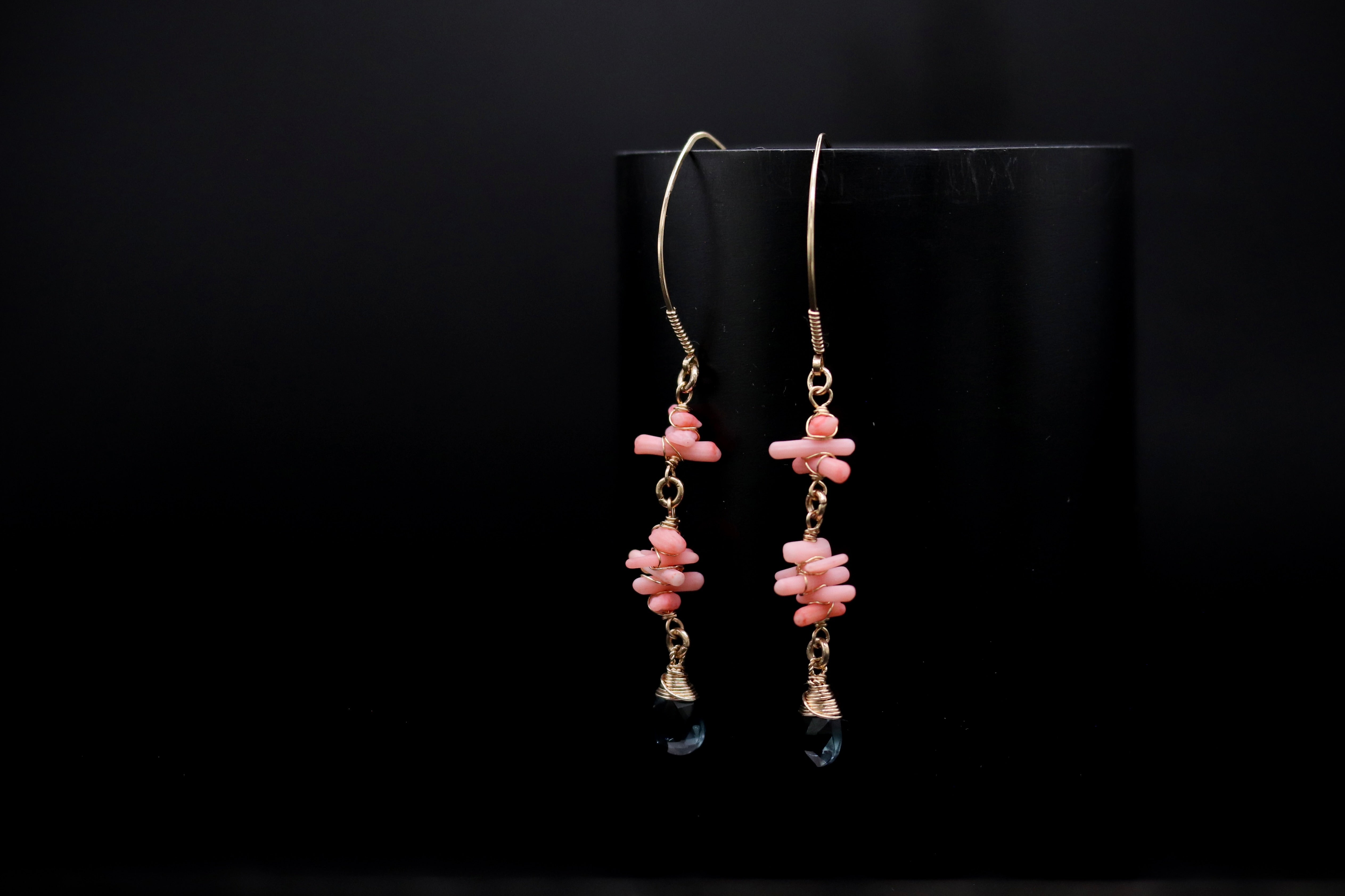 A pair of earrings with pink beads and black stones hanging from the bottom, displayed against a black background.