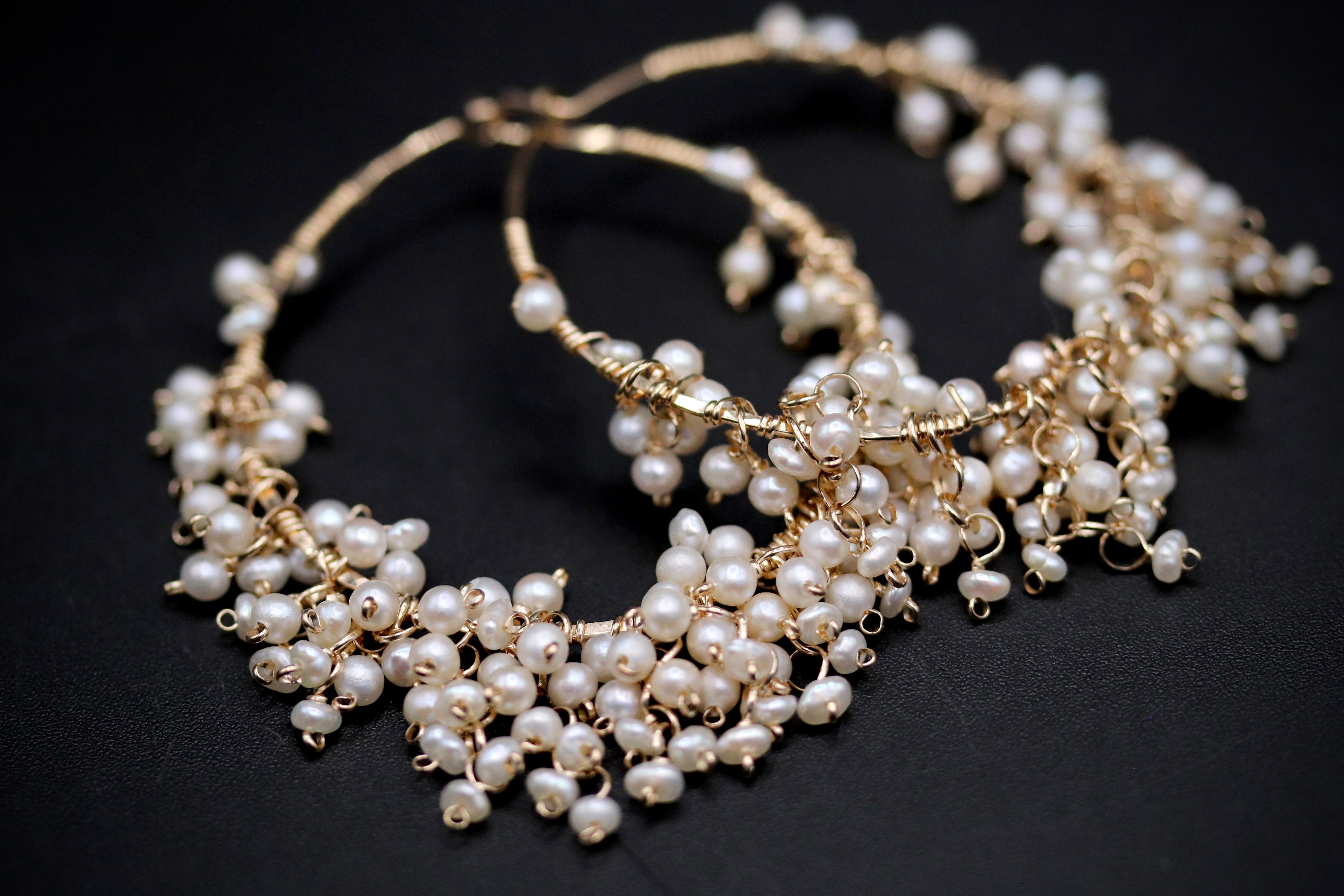 A close-up image of a pair of gold hoop earrings adorned with numerous small white pearls.