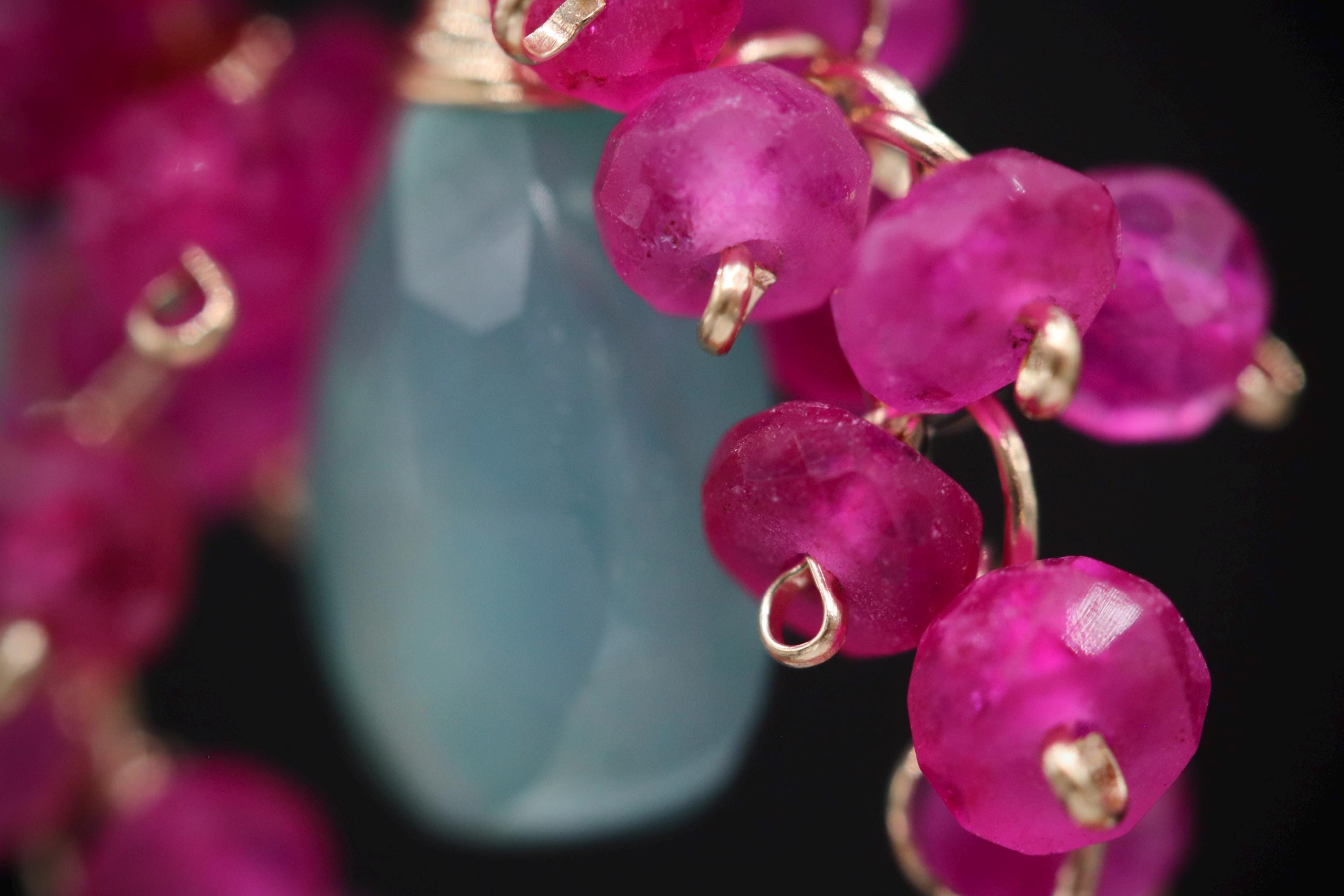 A close-up image of a necklace with a blue stone pendant and pink beads.