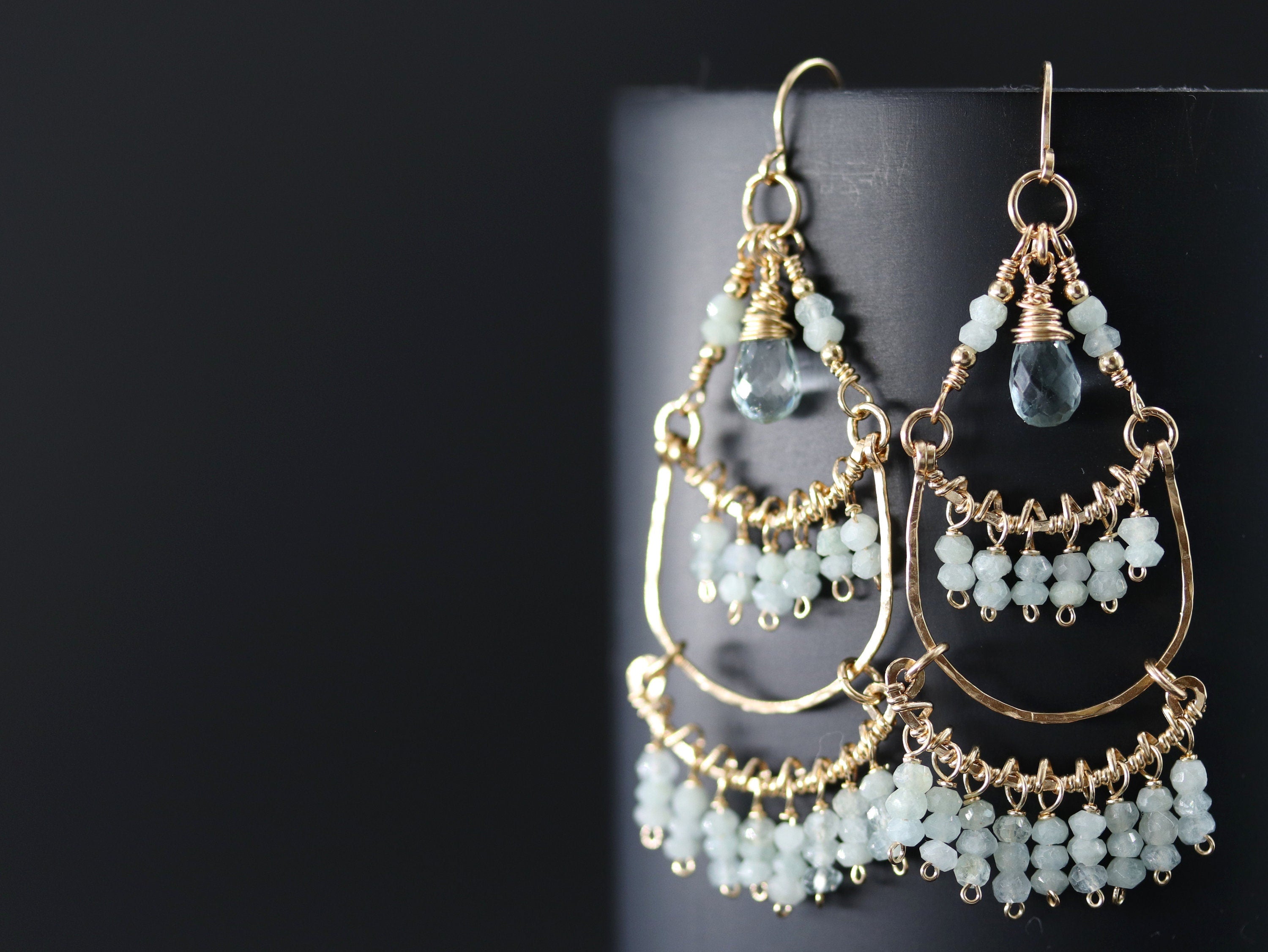 May include: Gold dangle earrings with a teardrop shaped light blue gemstone and multiple smaller light blue gemstones hanging from the bottom.