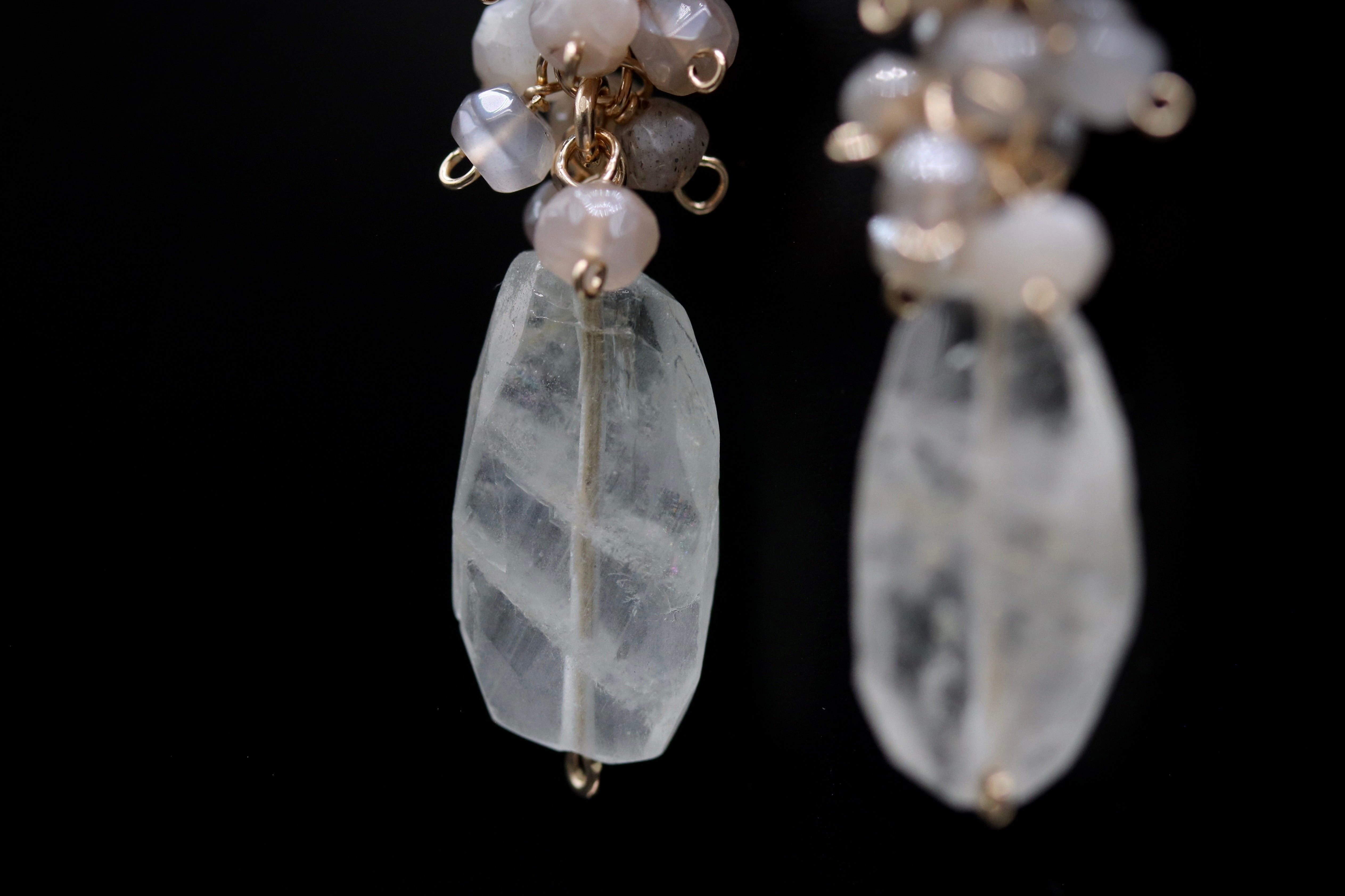 A close-up view of a pair of earrings with clear crystal stones and metal charms.