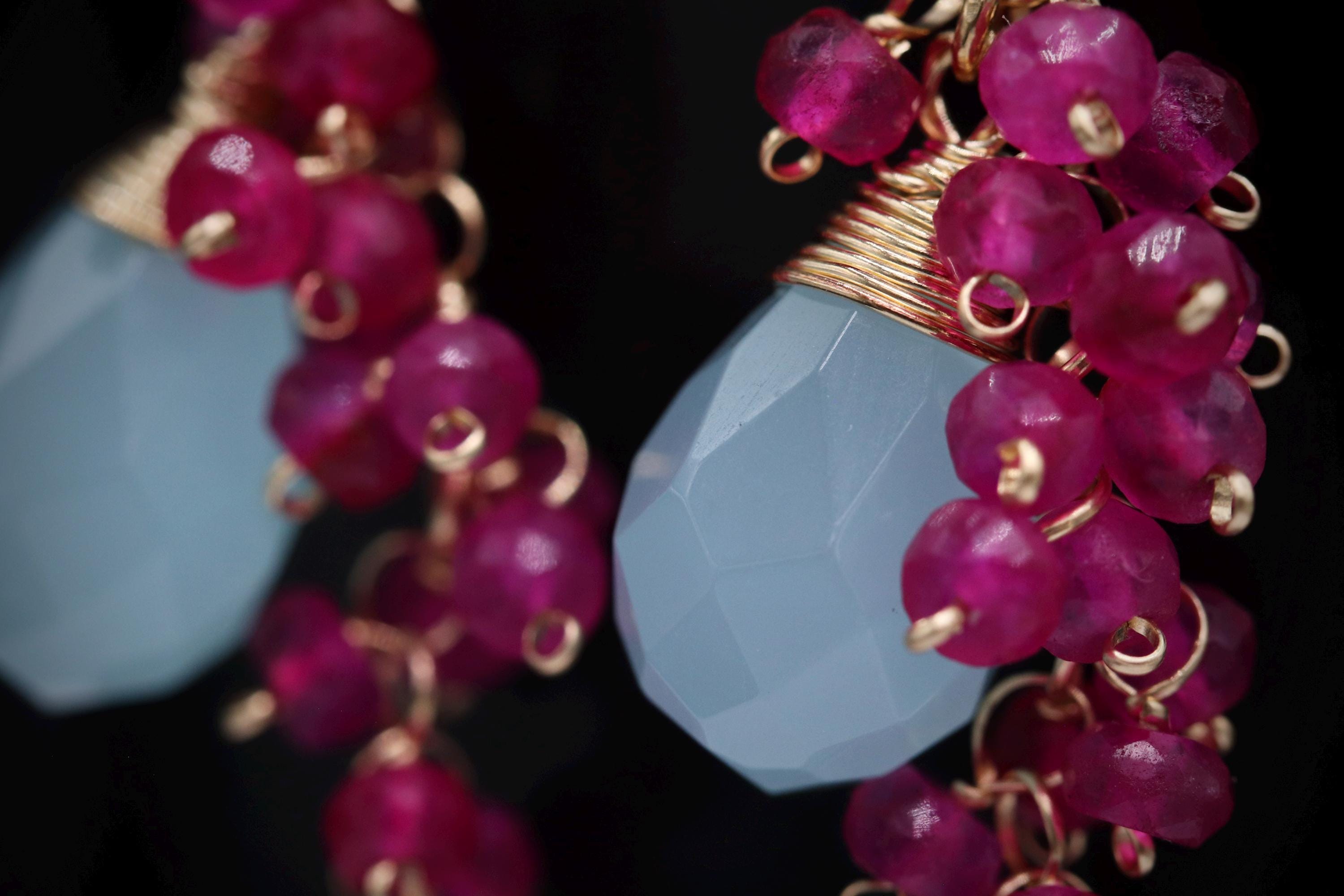 A close-up view of a pair of earrings with a combination of blue and pink gemstones, as well as gold-colored metal elements.