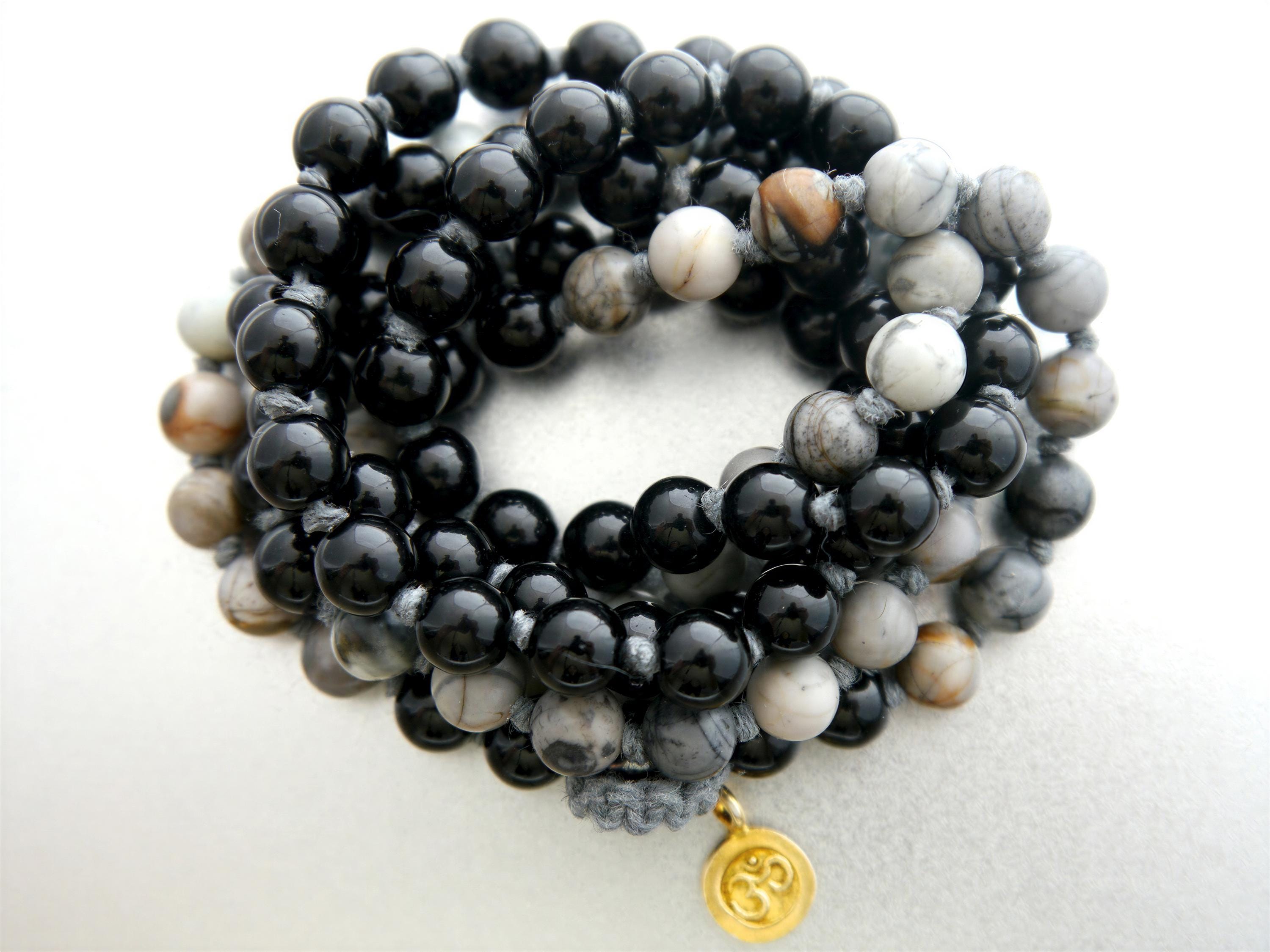 A close-up image of a beaded bracelet with black and gray stones, including a gold charm.