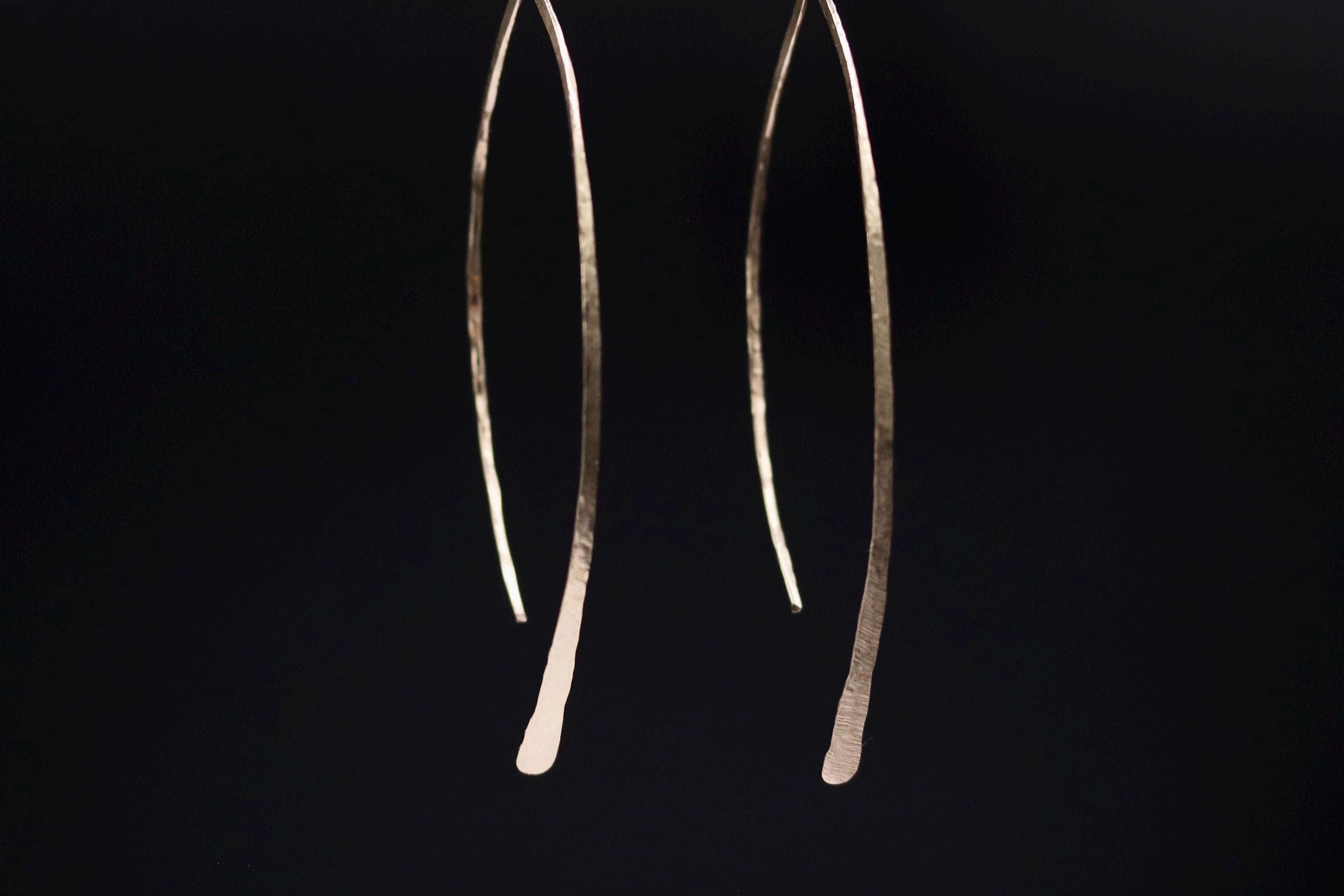 A pair of gold earrings with a curved design, hanging against a dark background.