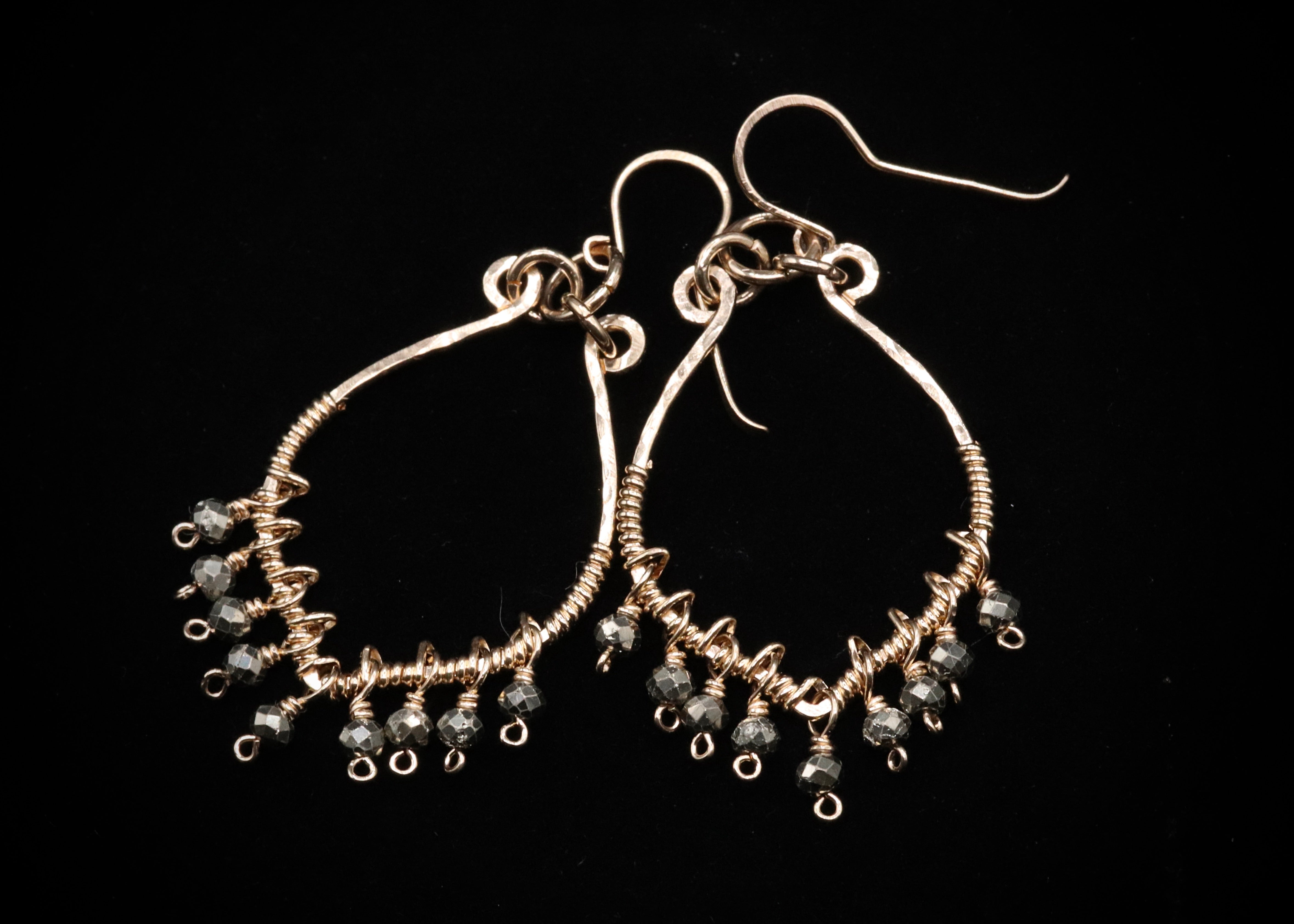 A pair of elegant earrings with a twisted metal design and small black beads hanging from the bottom.
