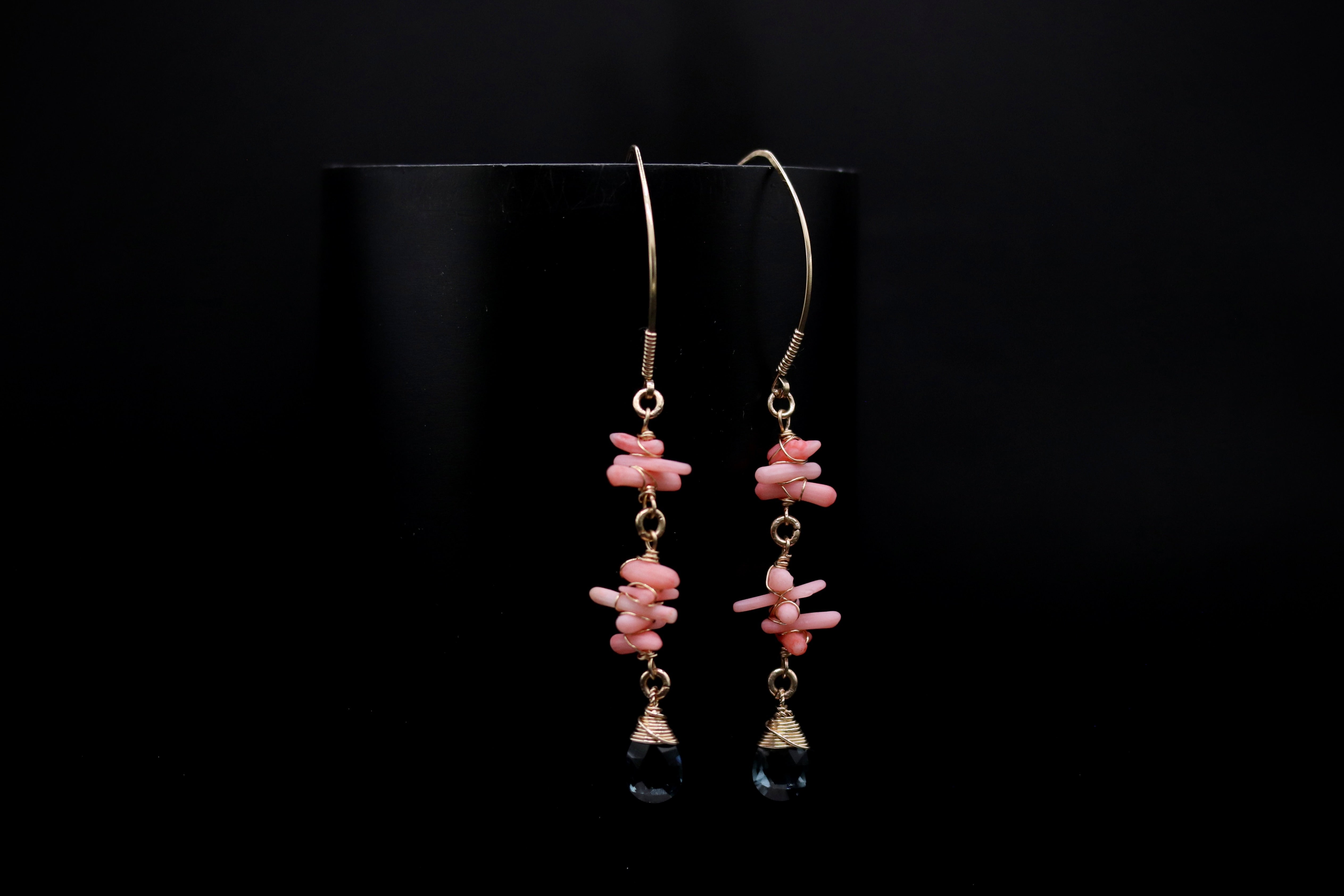 A pair of earrings with a combination of pink and black stones, hanging from a hook against a black background.