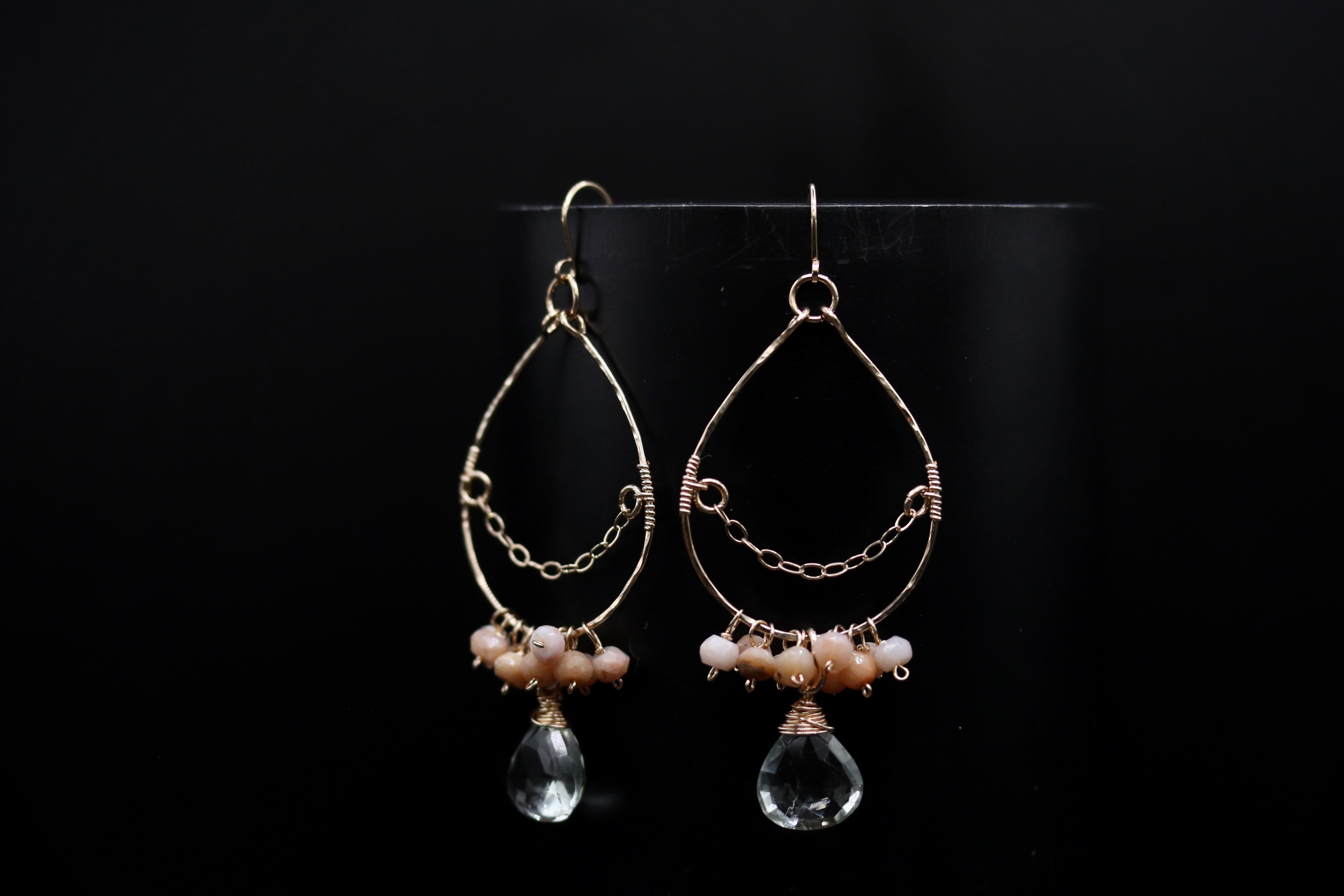 A pair of elegant earrings with a clear crystal pendant and beaded accents, displayed against a black background.