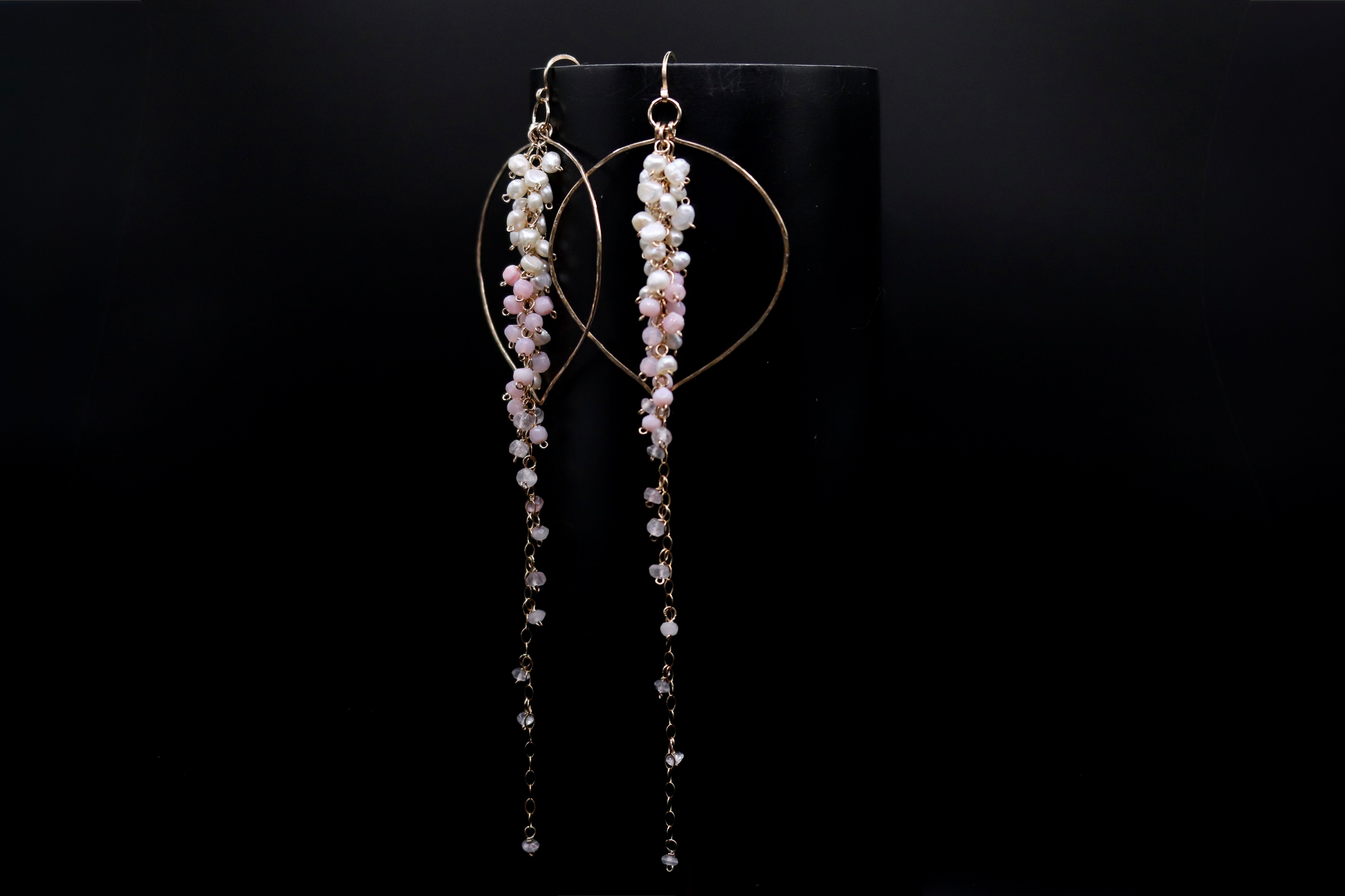 A pair of elegant earrings with long, dangling chains and small, white beads hanging from them, displayed against a black background.