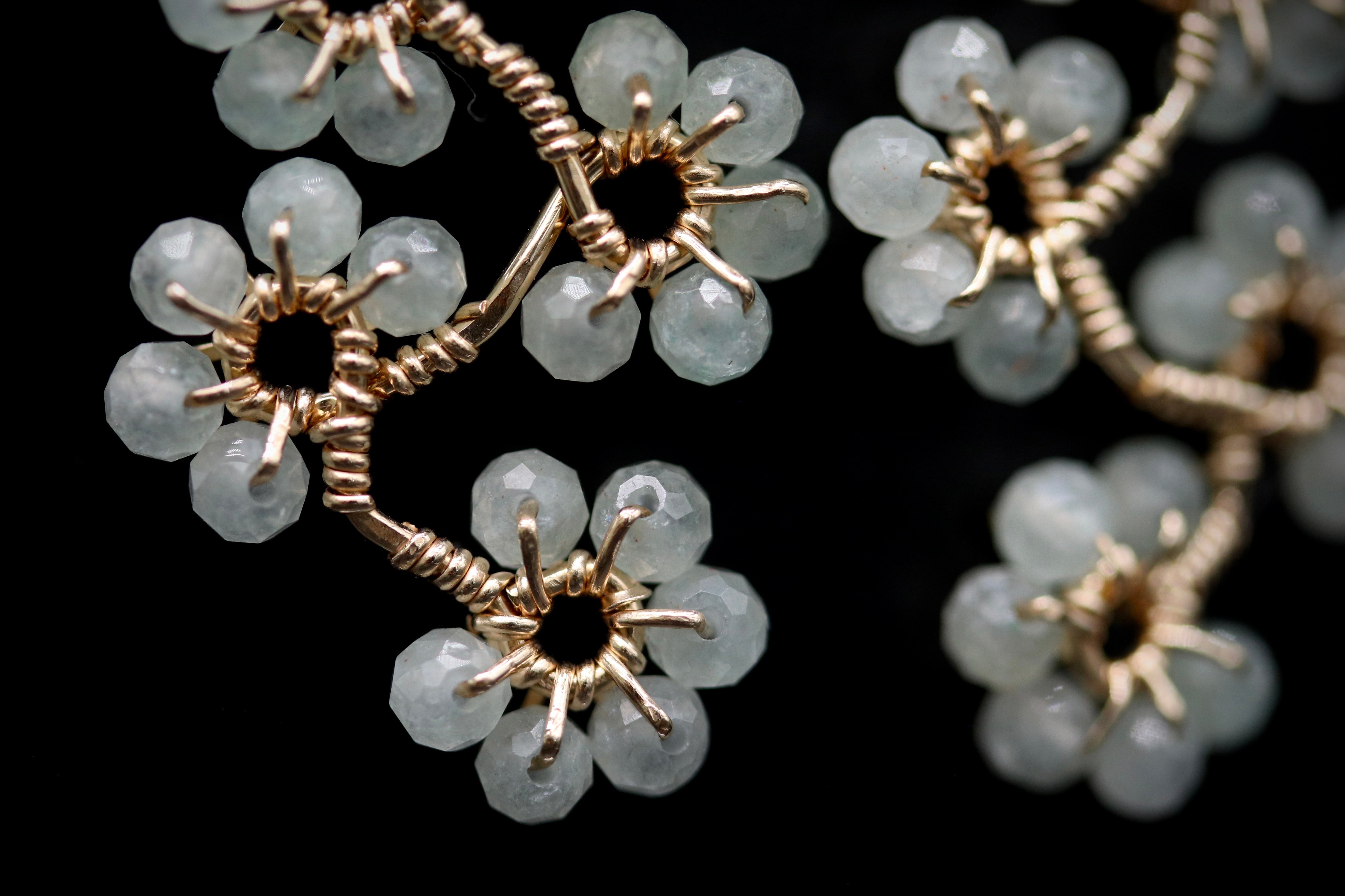 A close-up view of a delicate, intricate piece of jewelry composed of small, white, gemstone-like beads arranged in a floral pattern.