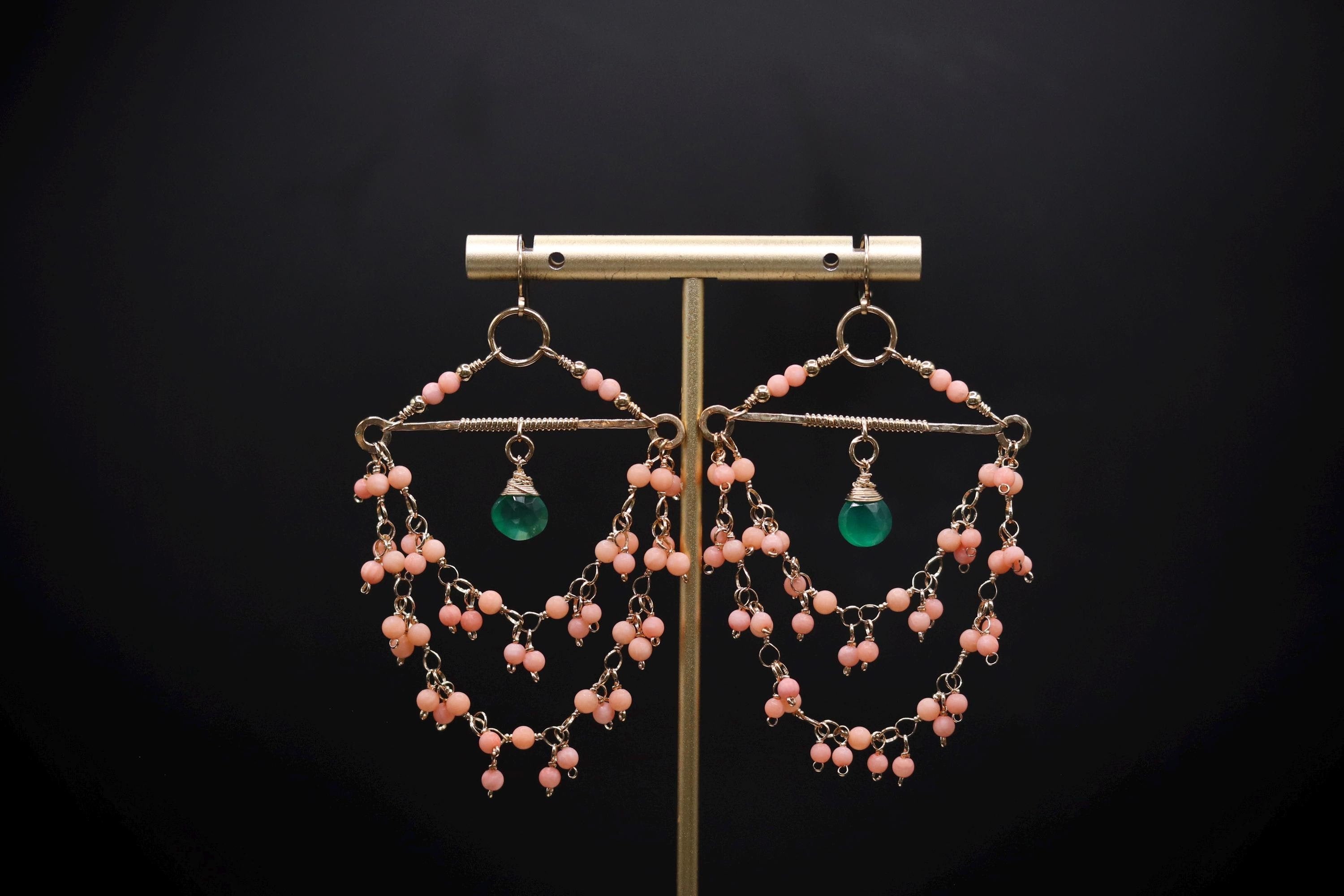 A pair of earrings with a gold metal frame and beaded designs, featuring a green gemstone and pink beads.