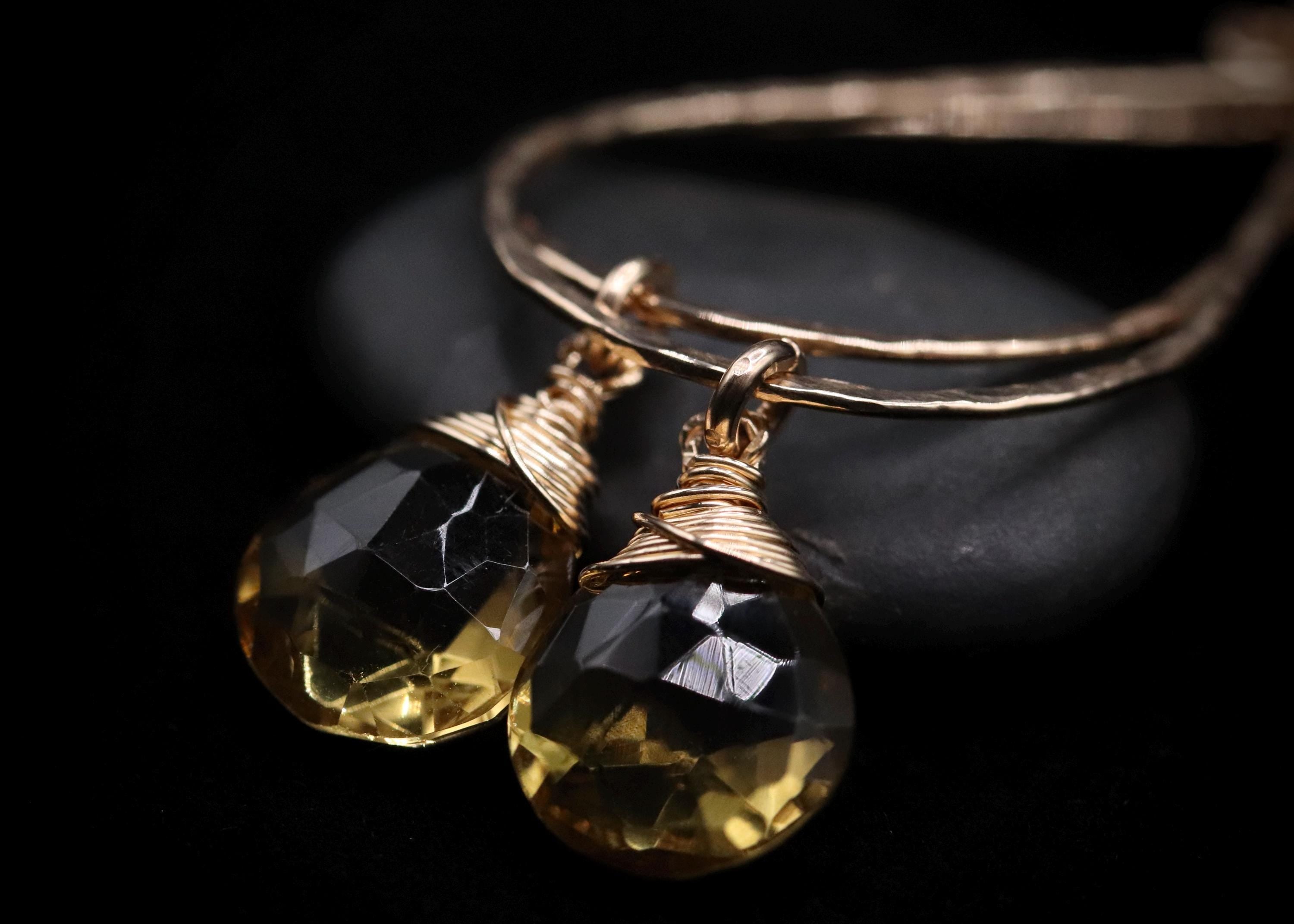 A pair of elegant gold-toned dangling earrings with clear gemstone pendants, resting on a dark surface.