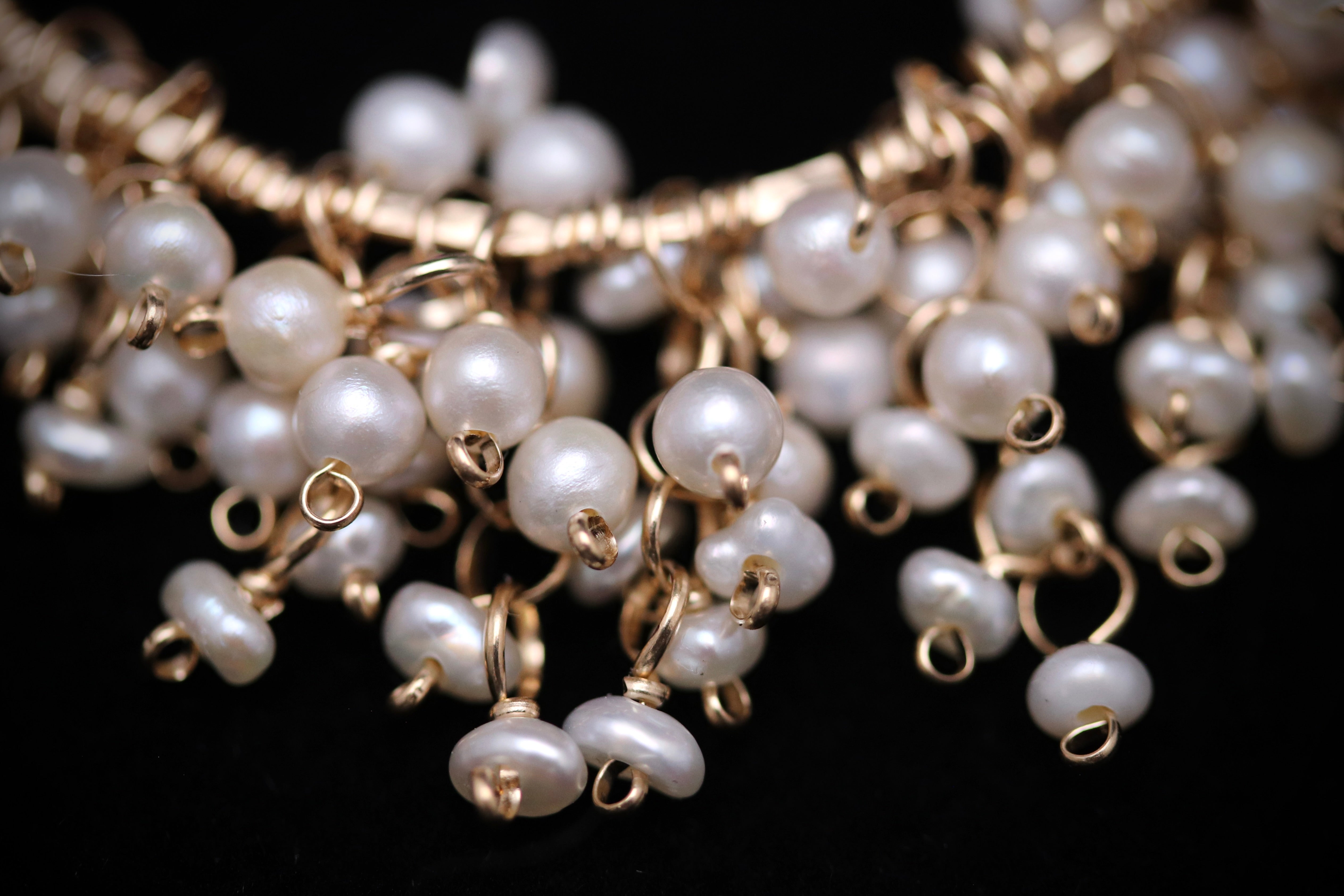 A close-up view of a delicate necklace made of numerous small, white pearls strung together with gold wire.