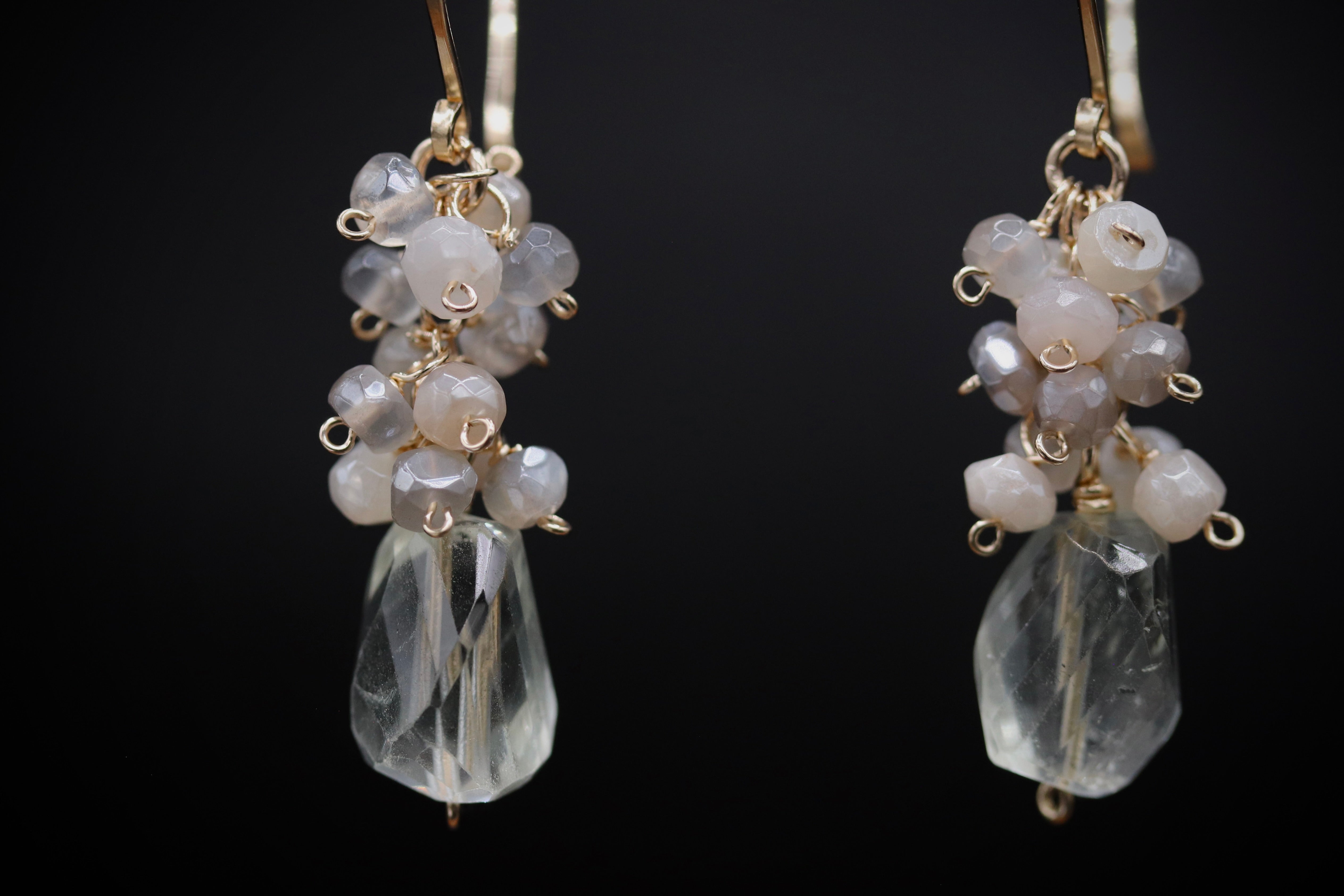 A pair of elegant earrings with clear gemstone beads and metal hooks against a dark background.