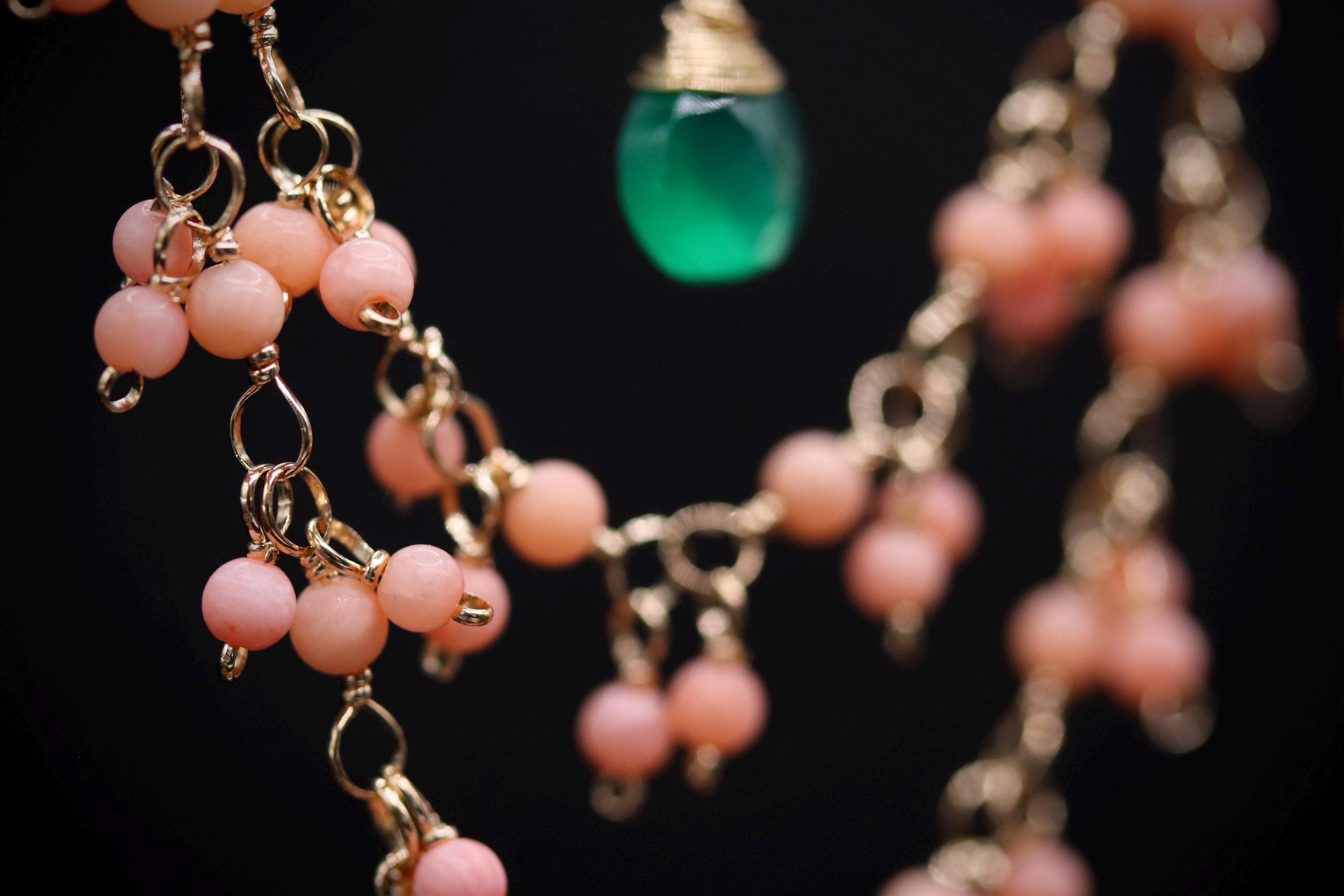 A close-up view of a necklace with a green pendant and a cluster of pink beads.