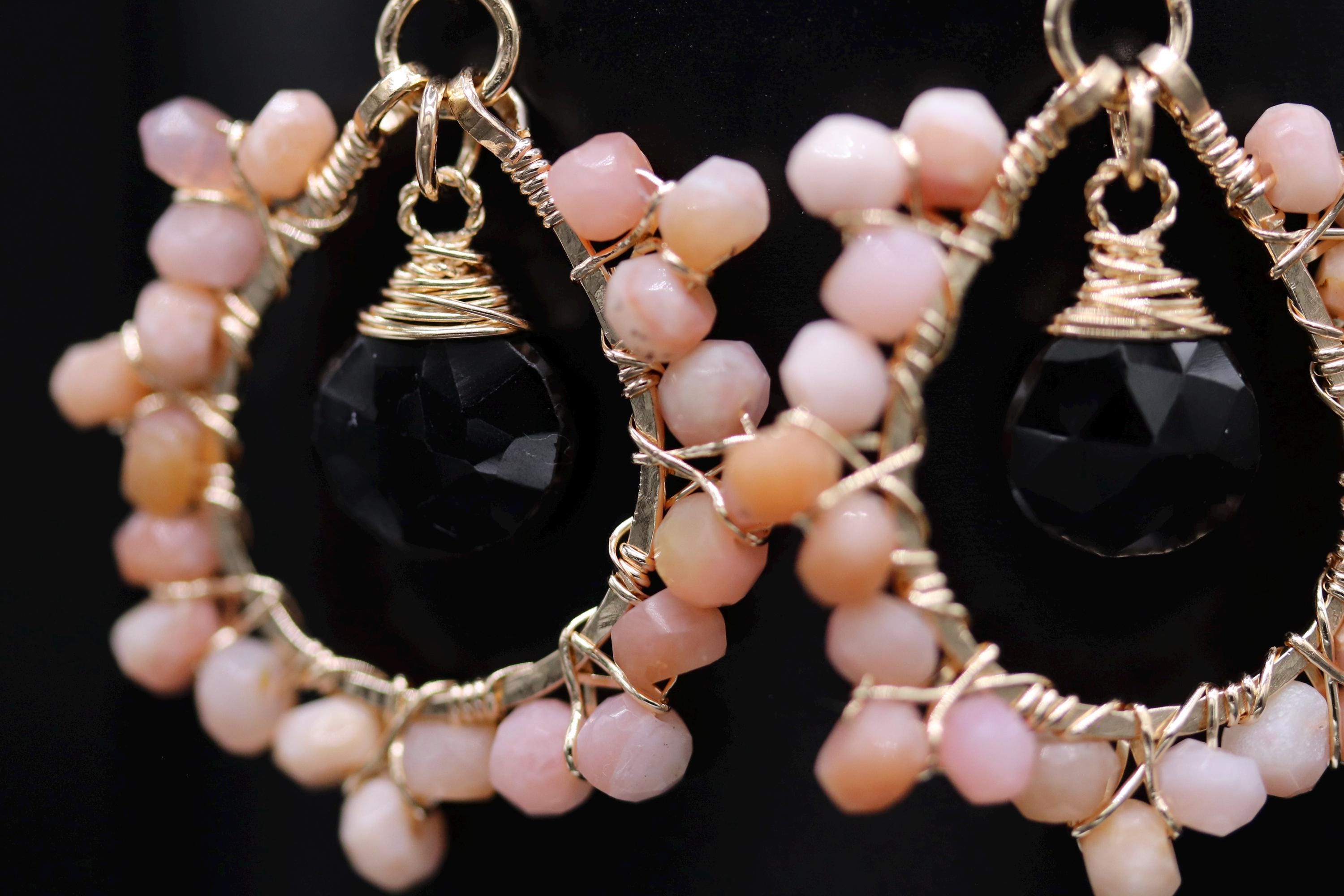 A close-up view of a pair of earrings with black and pink gemstone accents, set in a gold wire frame.