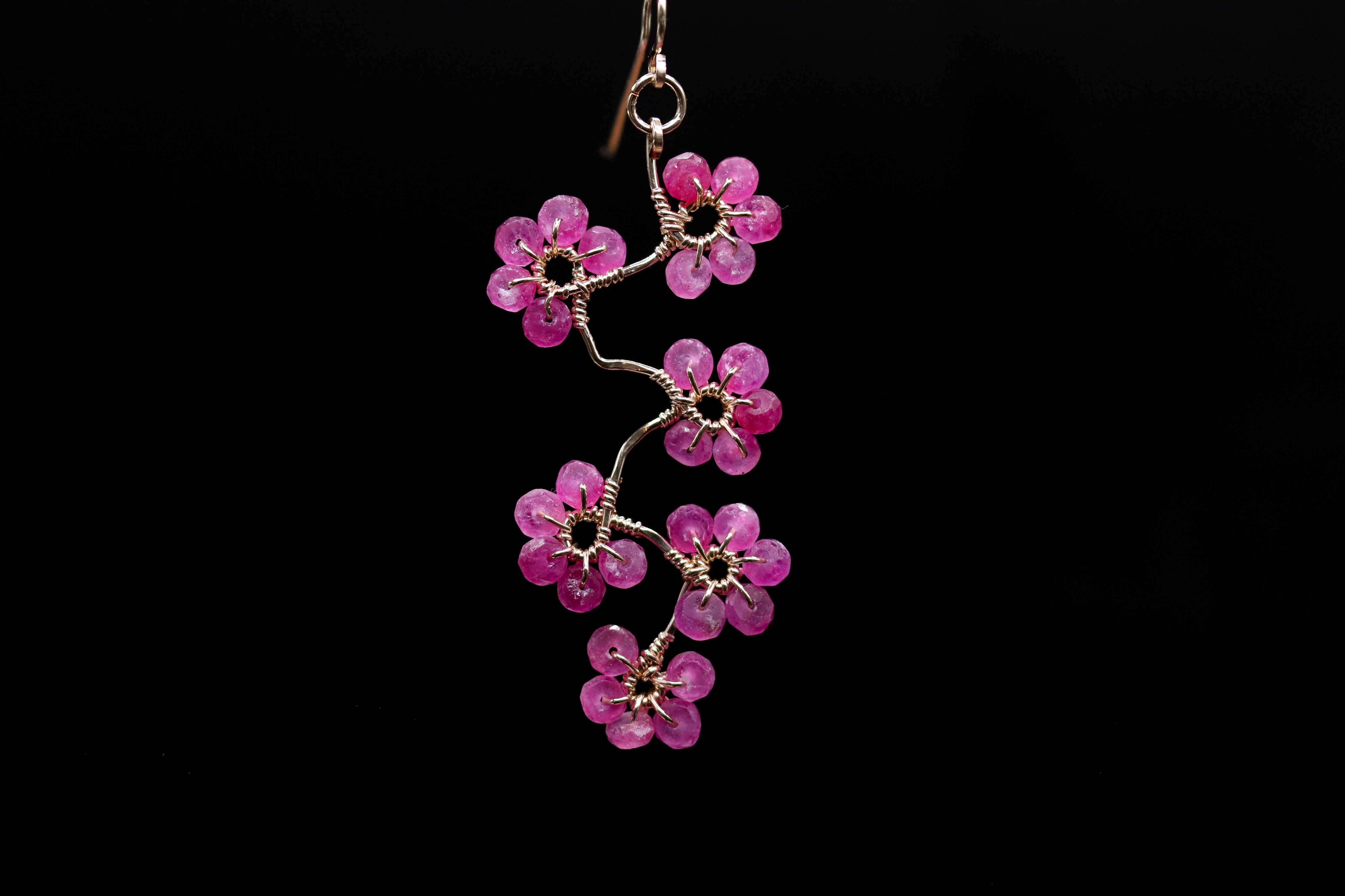 A delicate earring with a branch-like design made of small, pink beads or stones.