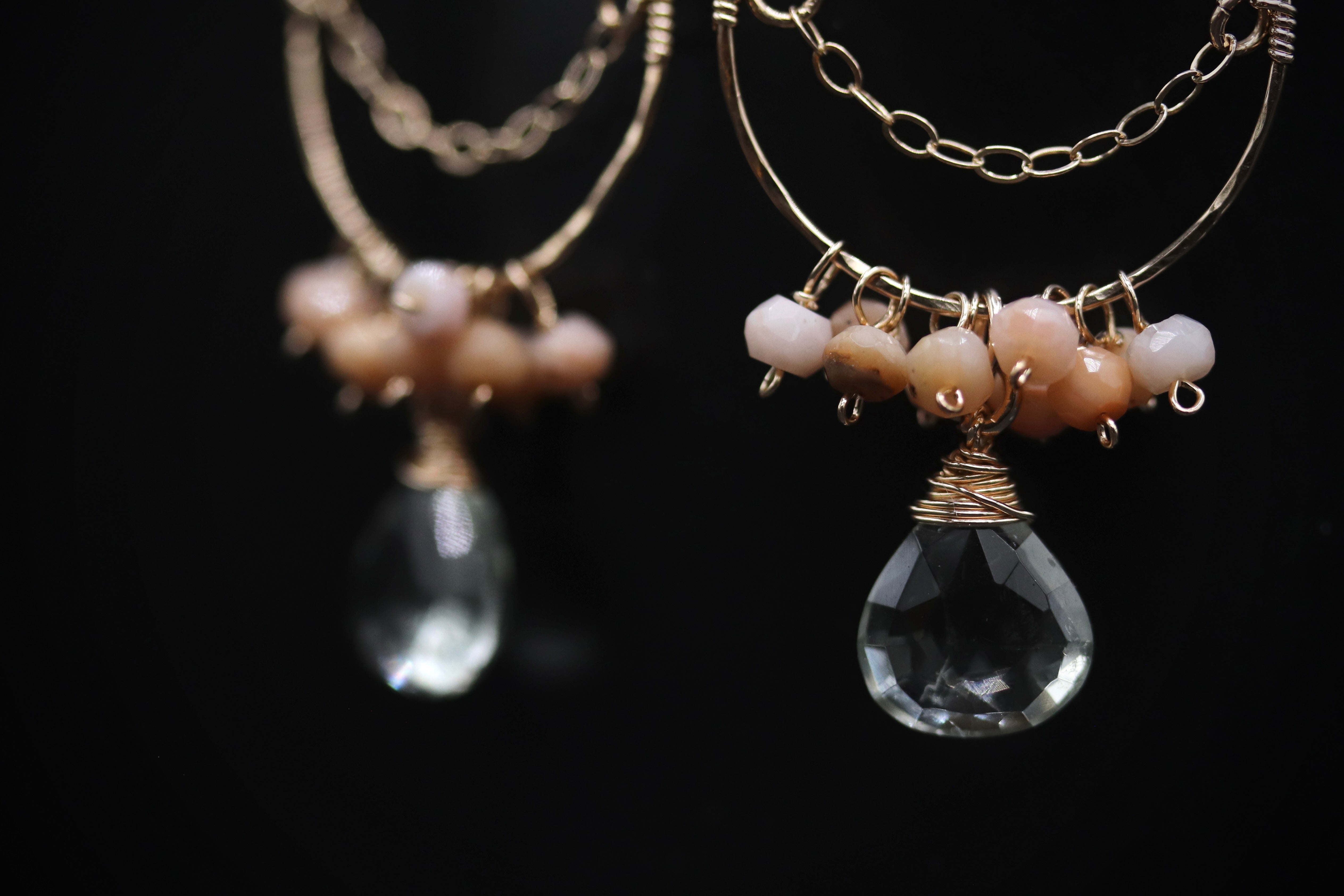 A pair of elegant earrings with clear gemstone pendants and metal chains against a black background.