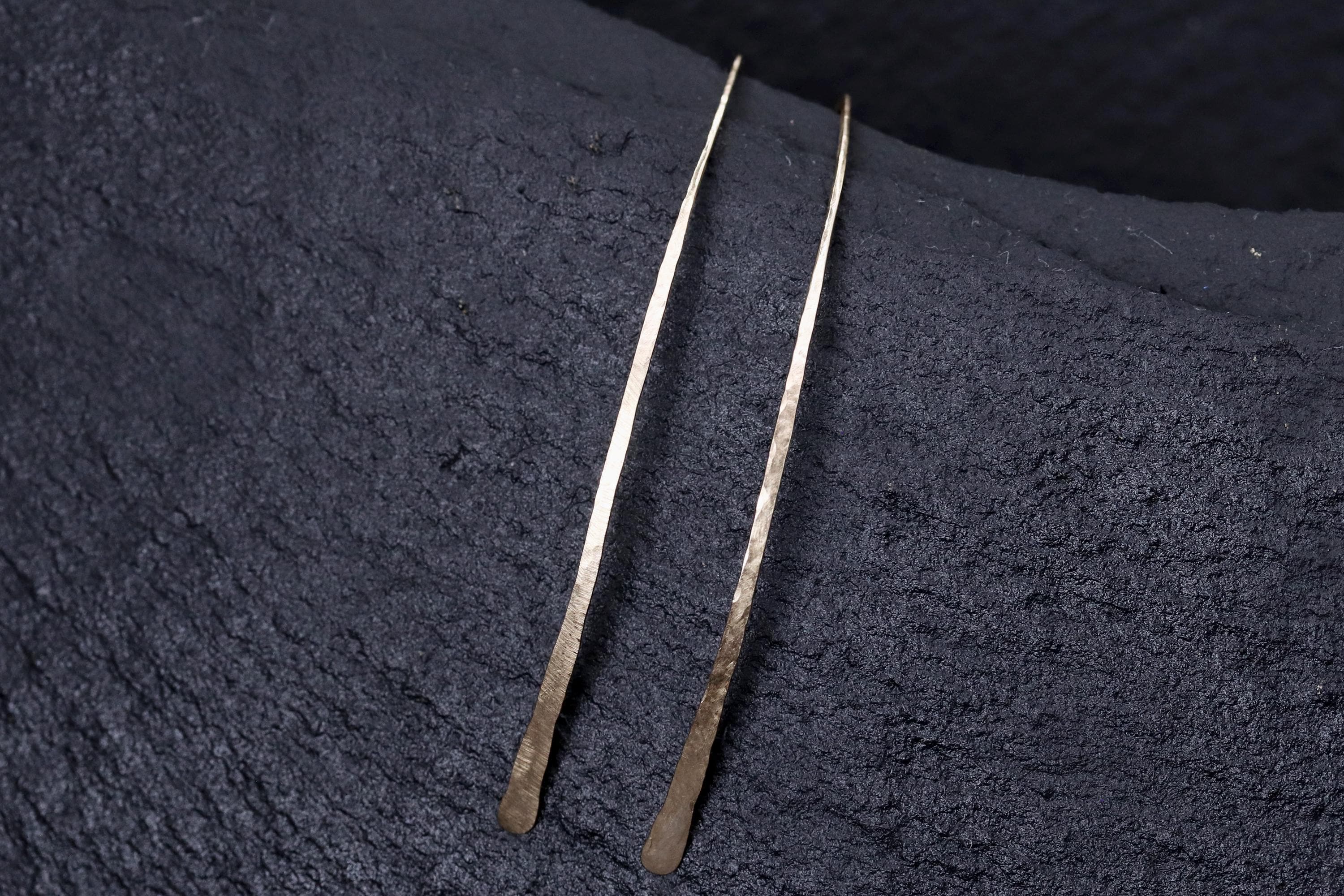 Two silver-colored metal objects, possibly earrings, are lying on a dark surface.