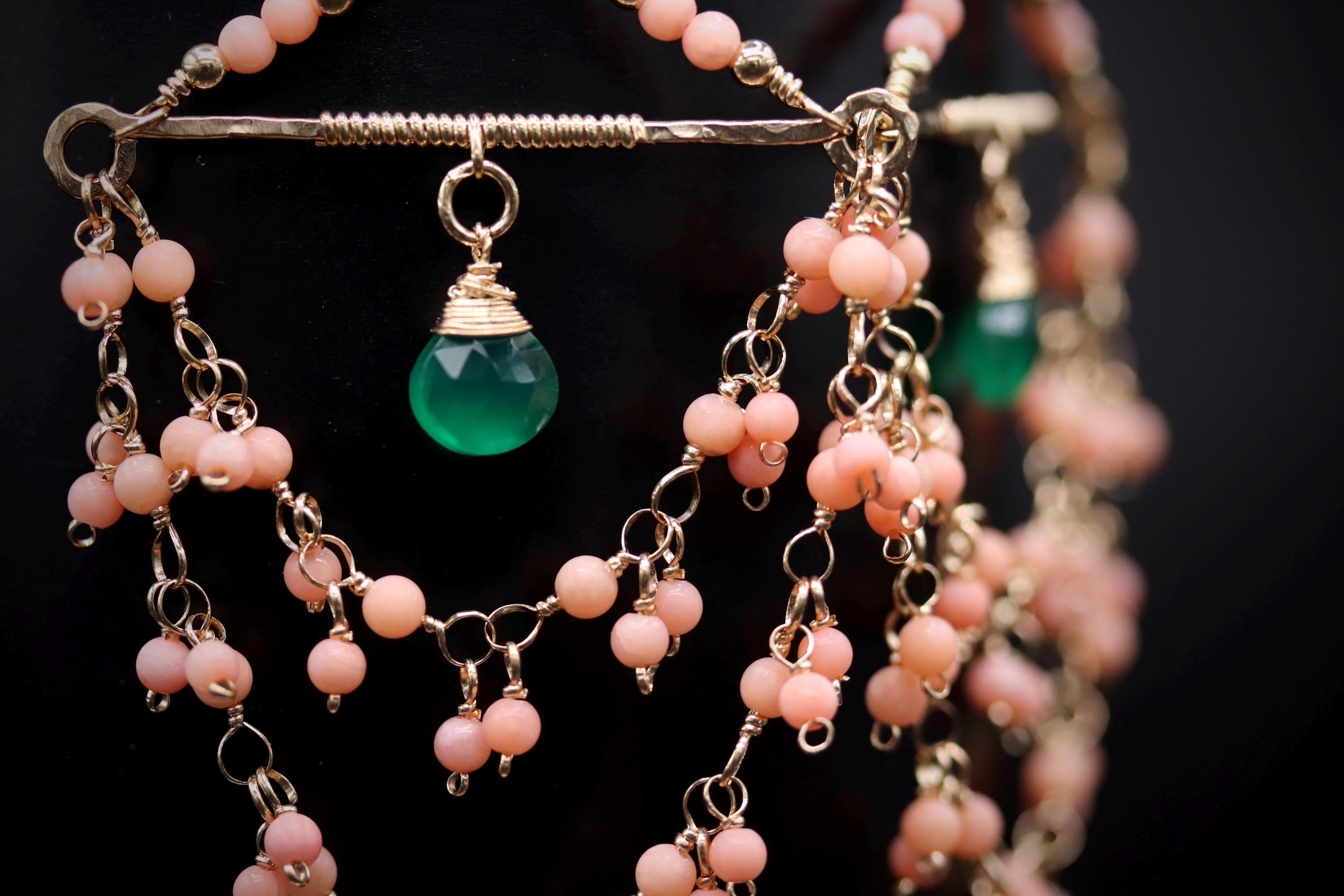 A close-up view of a delicate necklace with a green gemstone and numerous small, dangling beads in shades of pink and green.