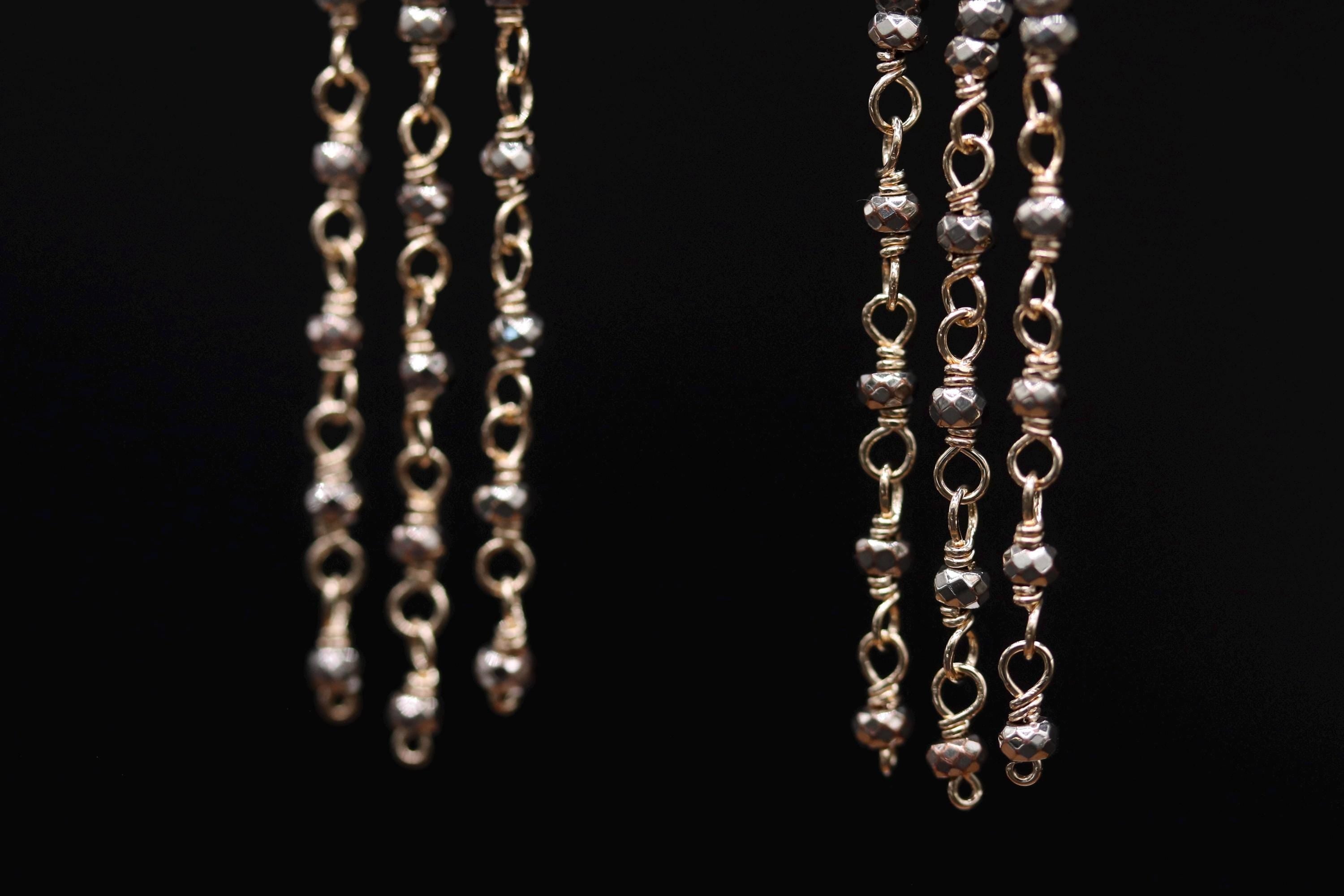 A close-up view of a pair of dangling earrings with a chain-like design, featuring small, round beads.