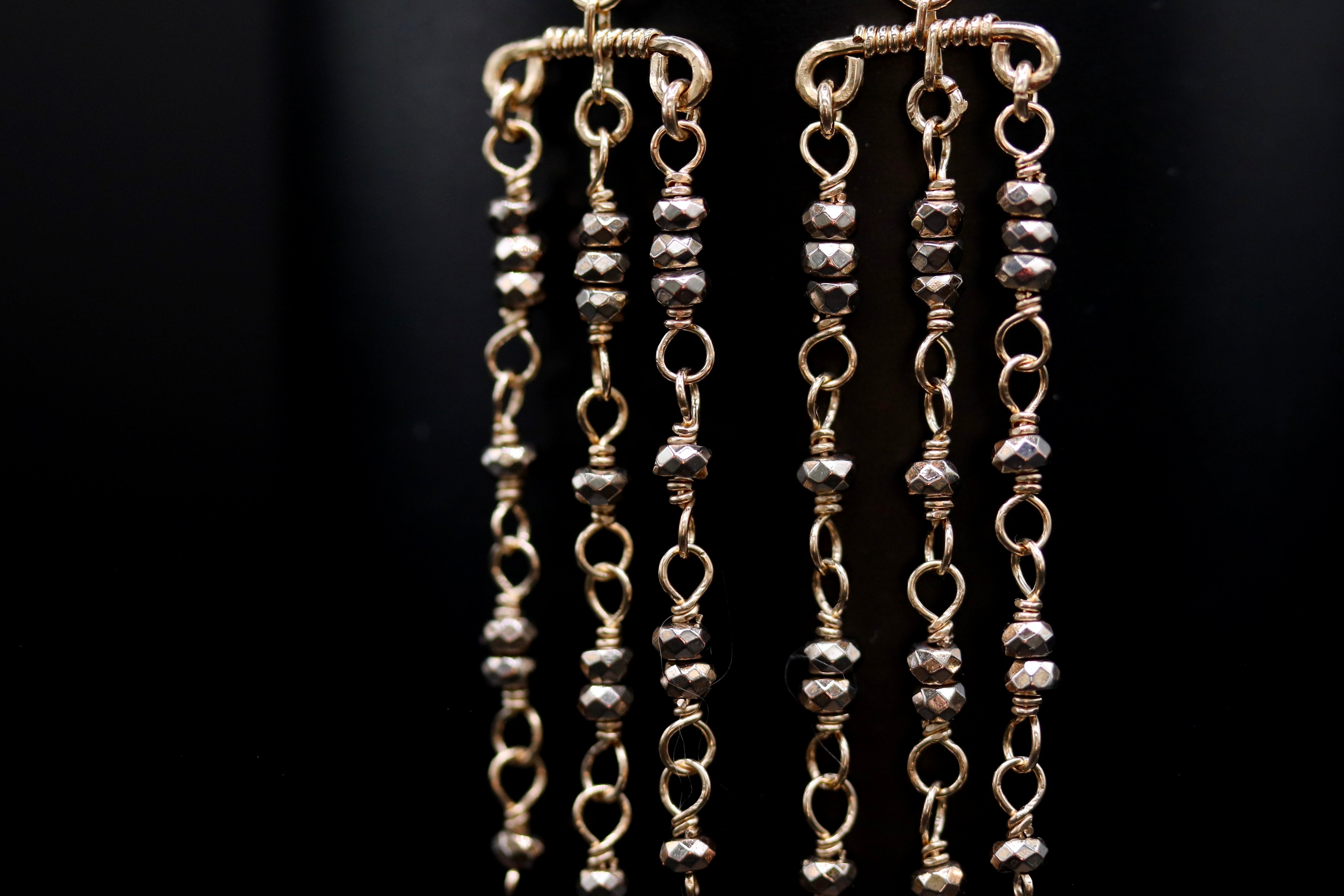 A close-up view of a pair of gold-colored earrings with multiple tiers of small, dangling beads.