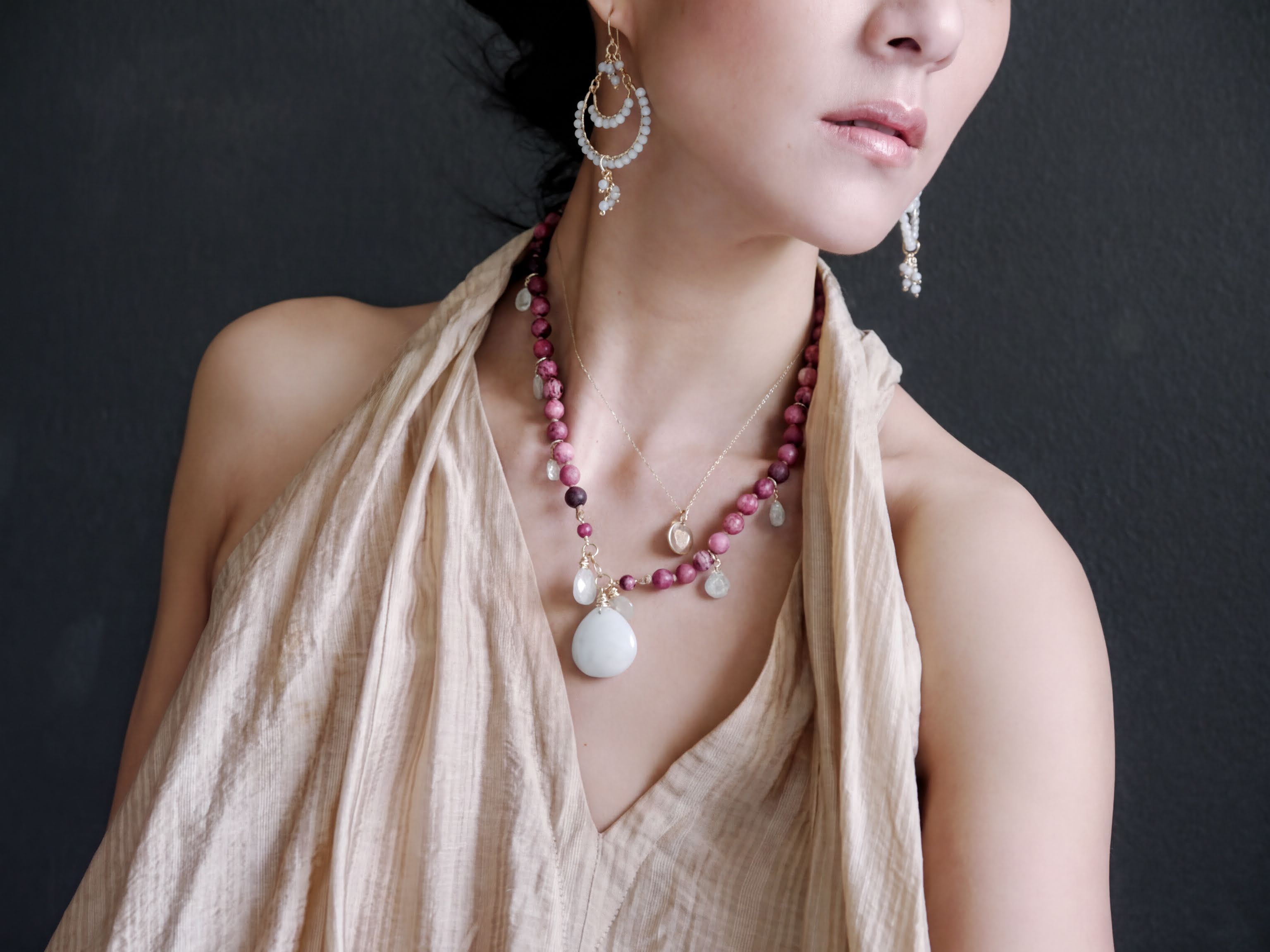 A woman wearing a beige dress and a necklace with various colorful beads and pendants, including a large white pendant.